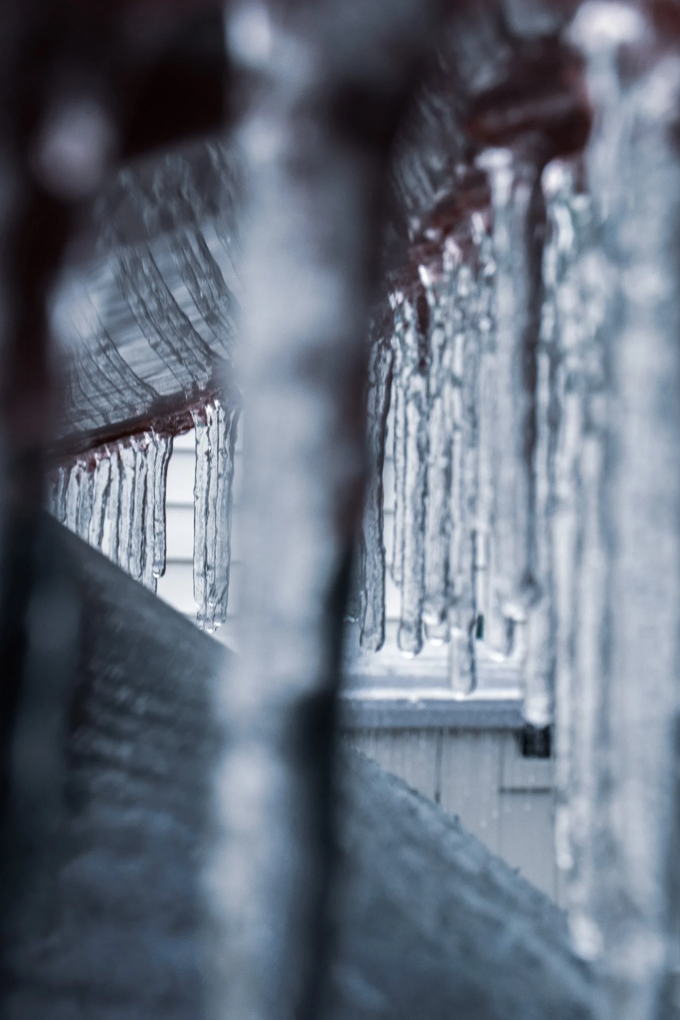 Close-up of icicles hanging from a surface near a window, with a blurry background.