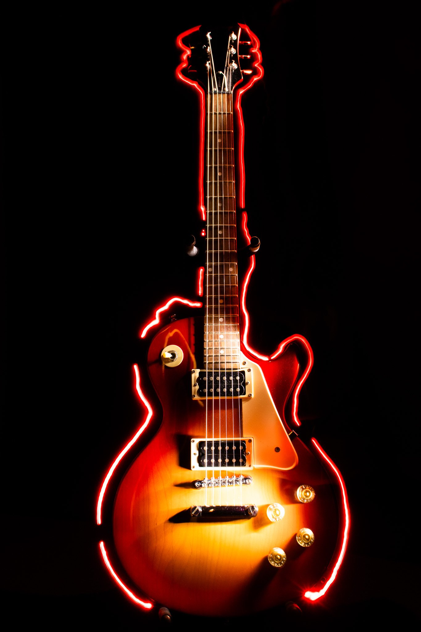 Electric guitar with a sunburst finish surrounded by red neon light accents.