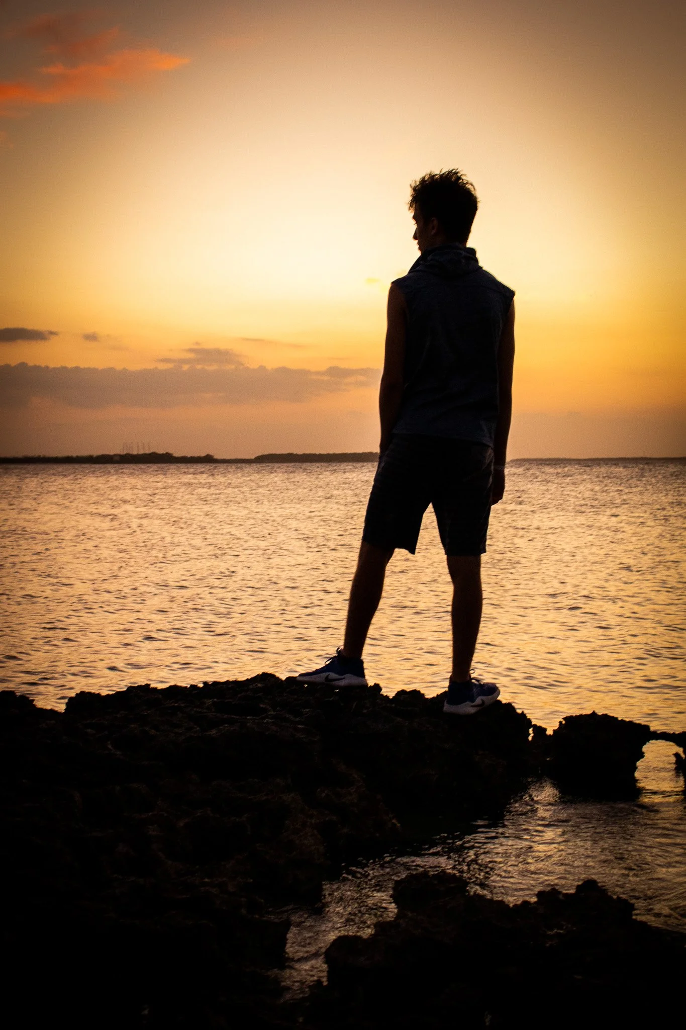 Silhouette of a person standing on rocks by the water during sunset.