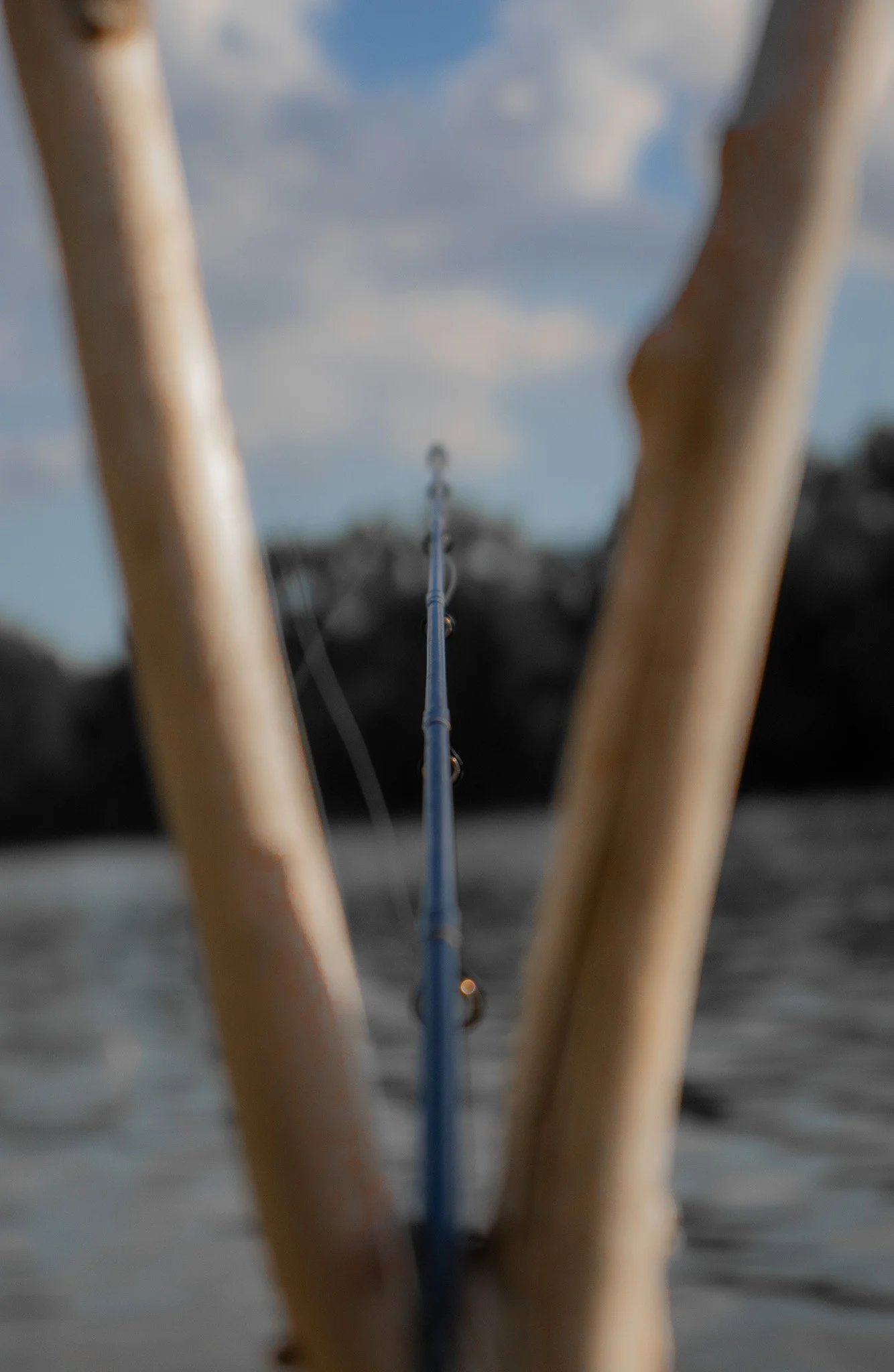 View from a boat or dock looking into the water at a fishing line or rod extending into the water, with a cloudy sky reflected on the water surface.