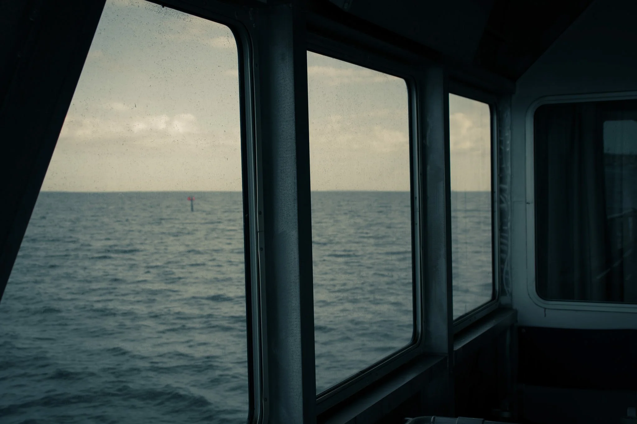 View through windows of a boat showing the ocean with a small red buoy in the distance during daytime.