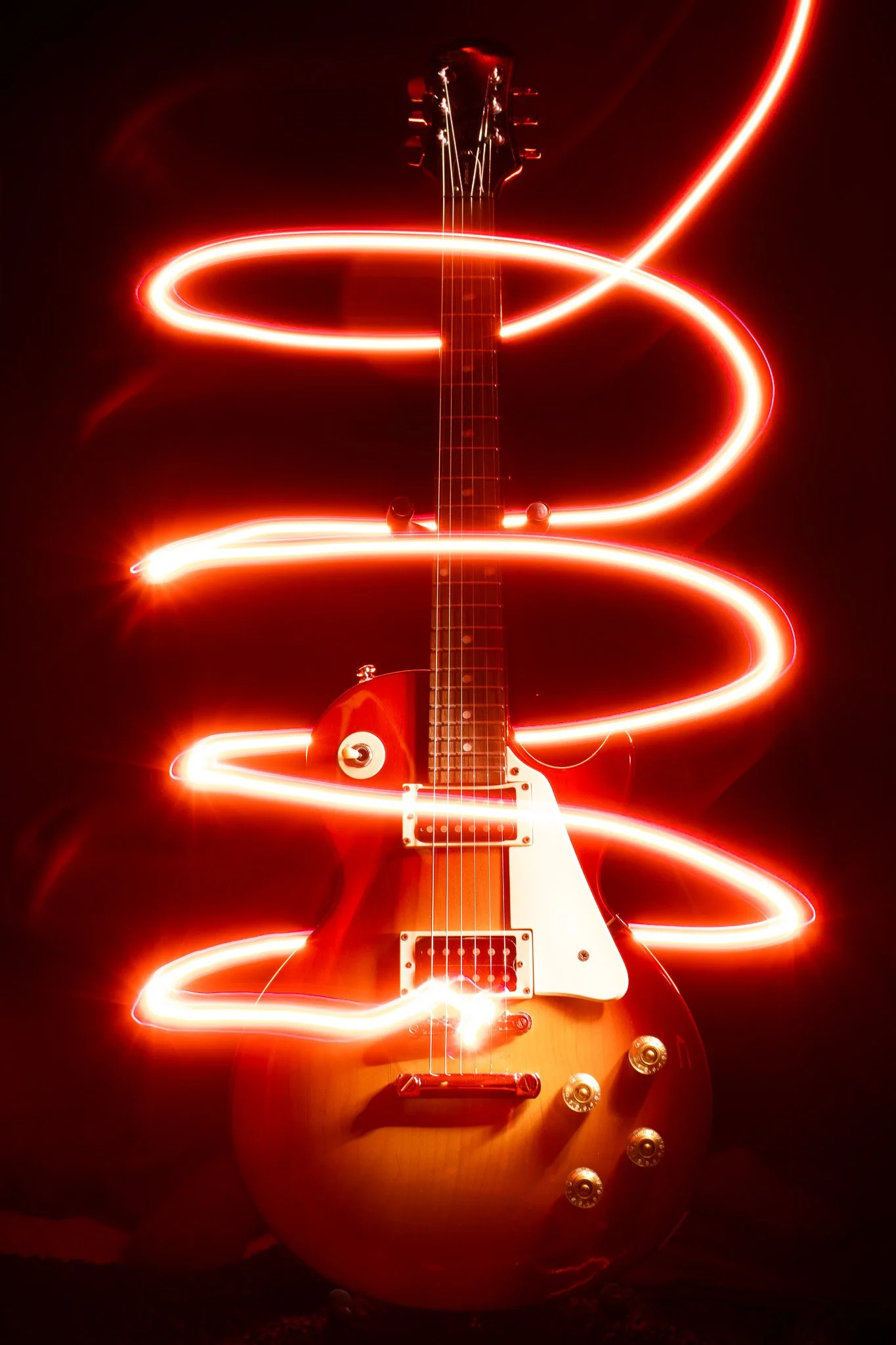 Electric guitar with red light trails swirling around it in a dark setting.
