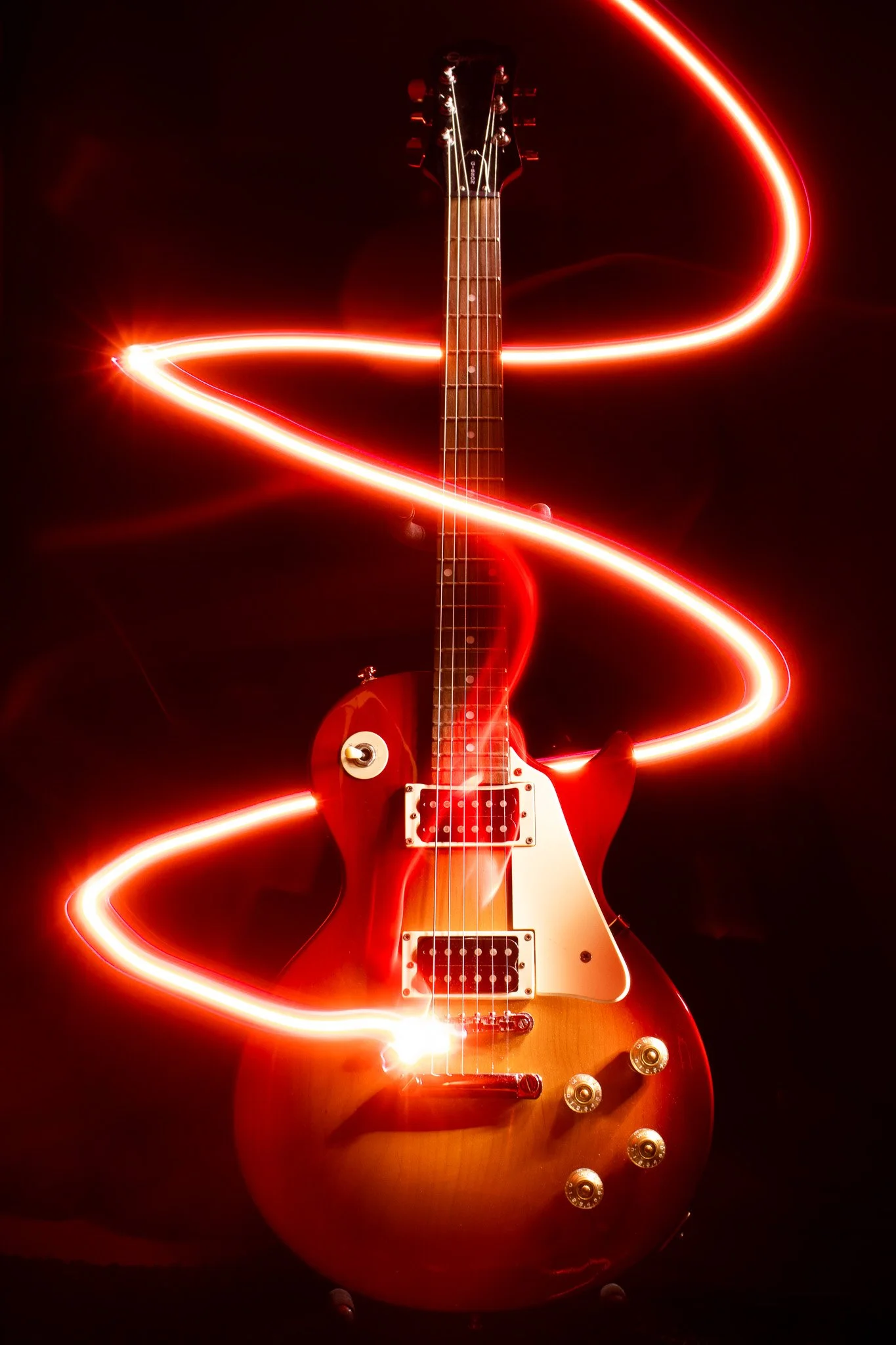 Red electric guitar against black background with red light trails swirling around it.