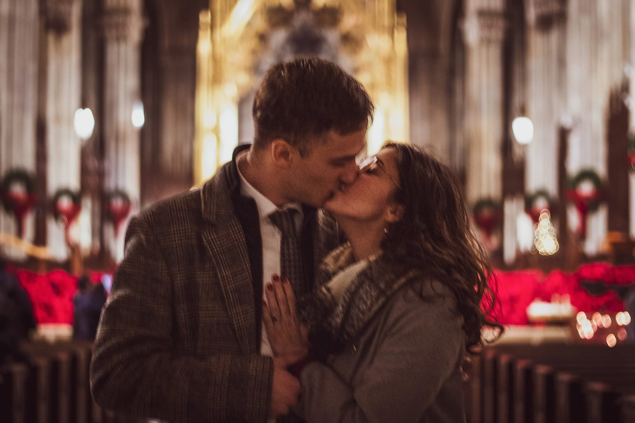 A couple sharing a kiss inside a Christmas decorated church with red poinsettias and wreaths