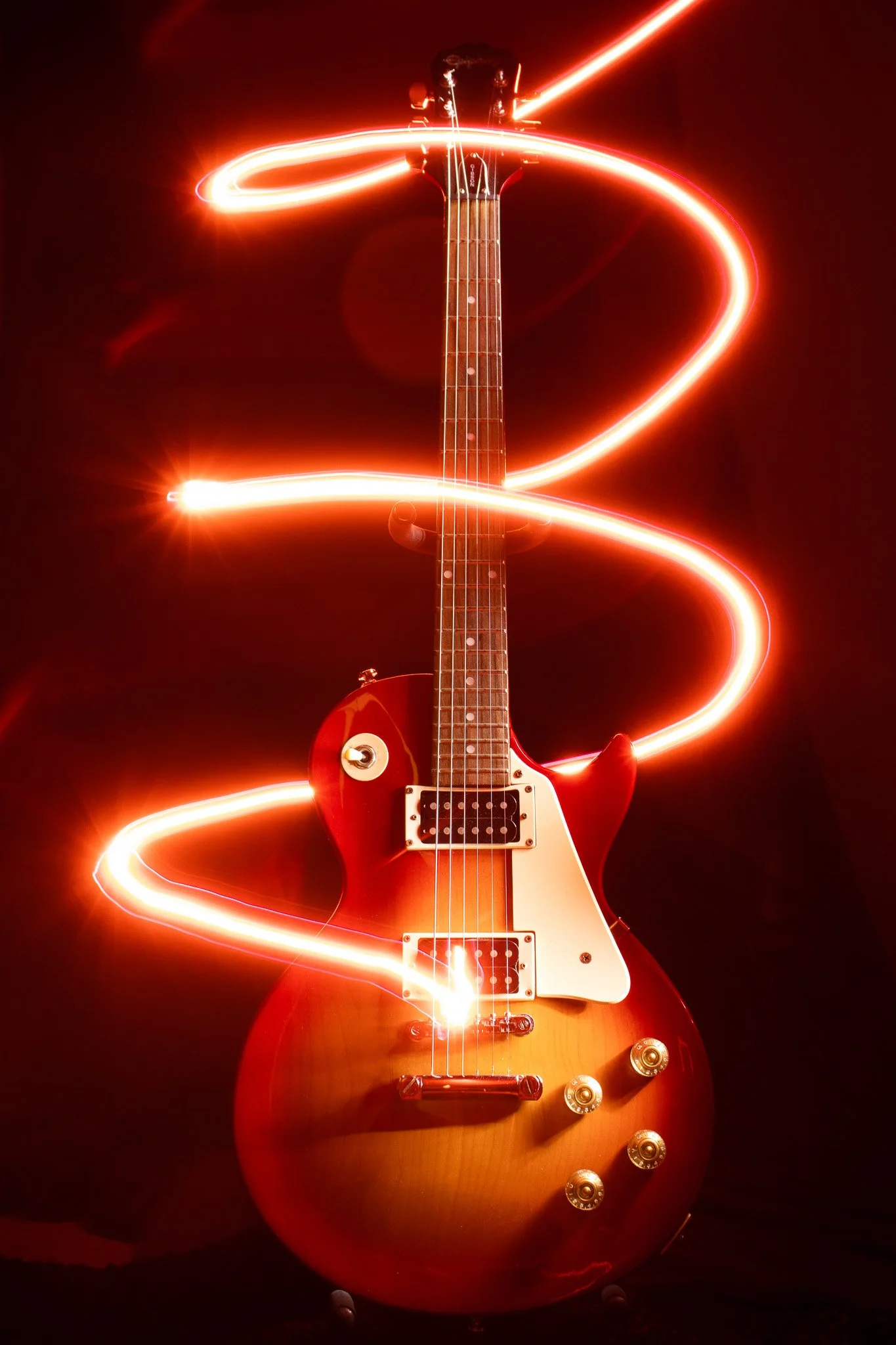 An electric guitar with light trails swirling around it against a dark background.