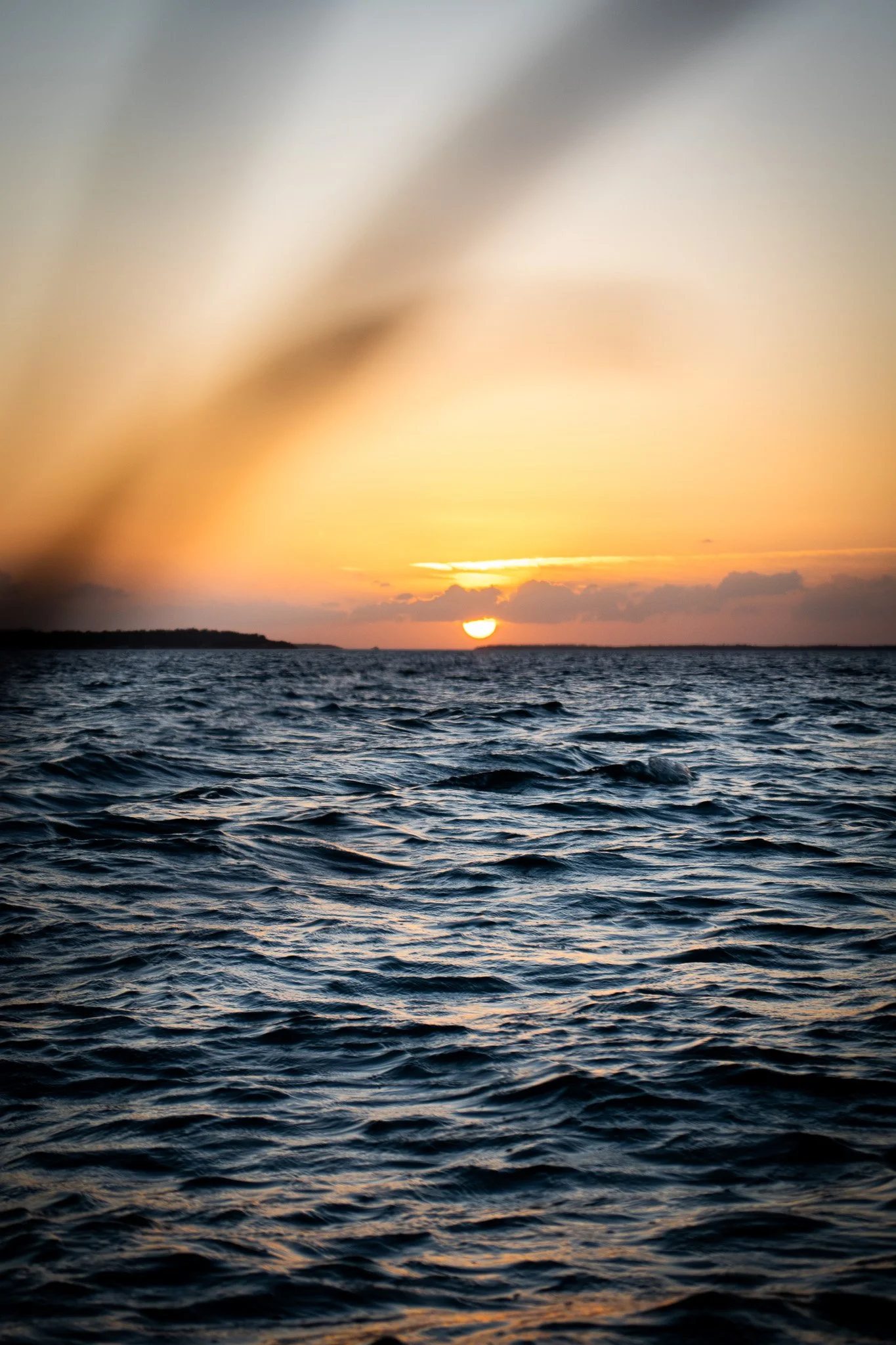 Sunset over the ocean with dark waves, orange and yellow sky, and clouds.