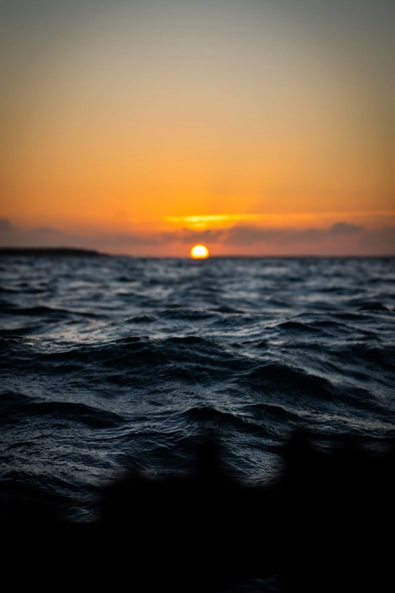 Sunset over the ocean with the sun near the horizon and waves in the foreground.