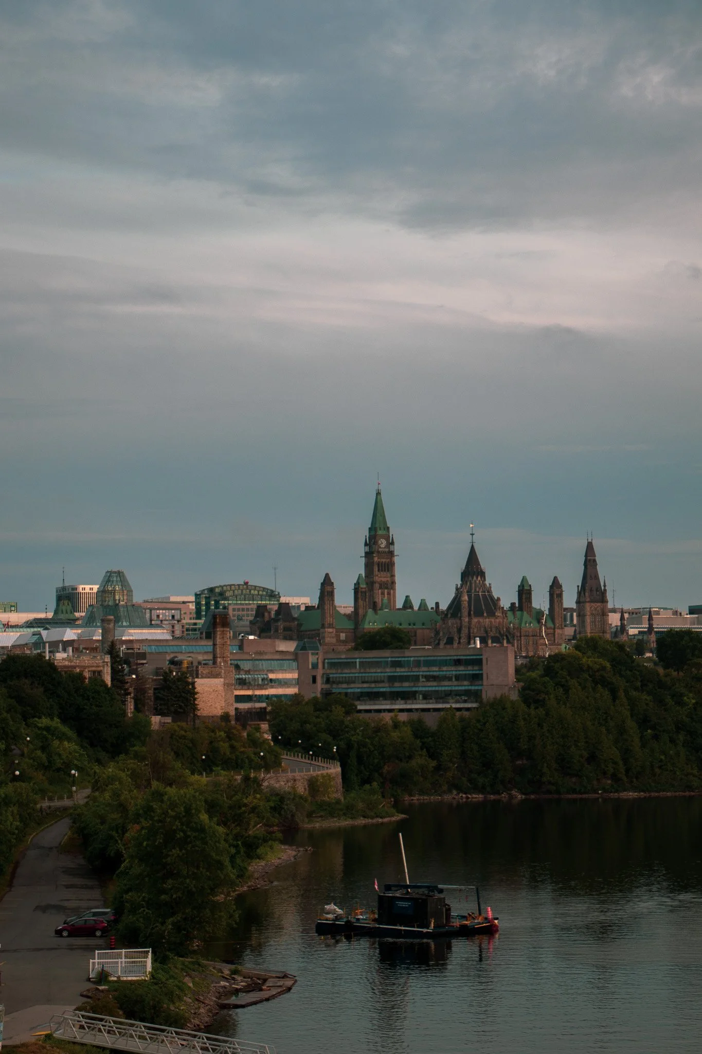 Photo of the Ottawa, Canada skyline with historic buildings, a cloudy sky, and a boat on the river in the foreground.