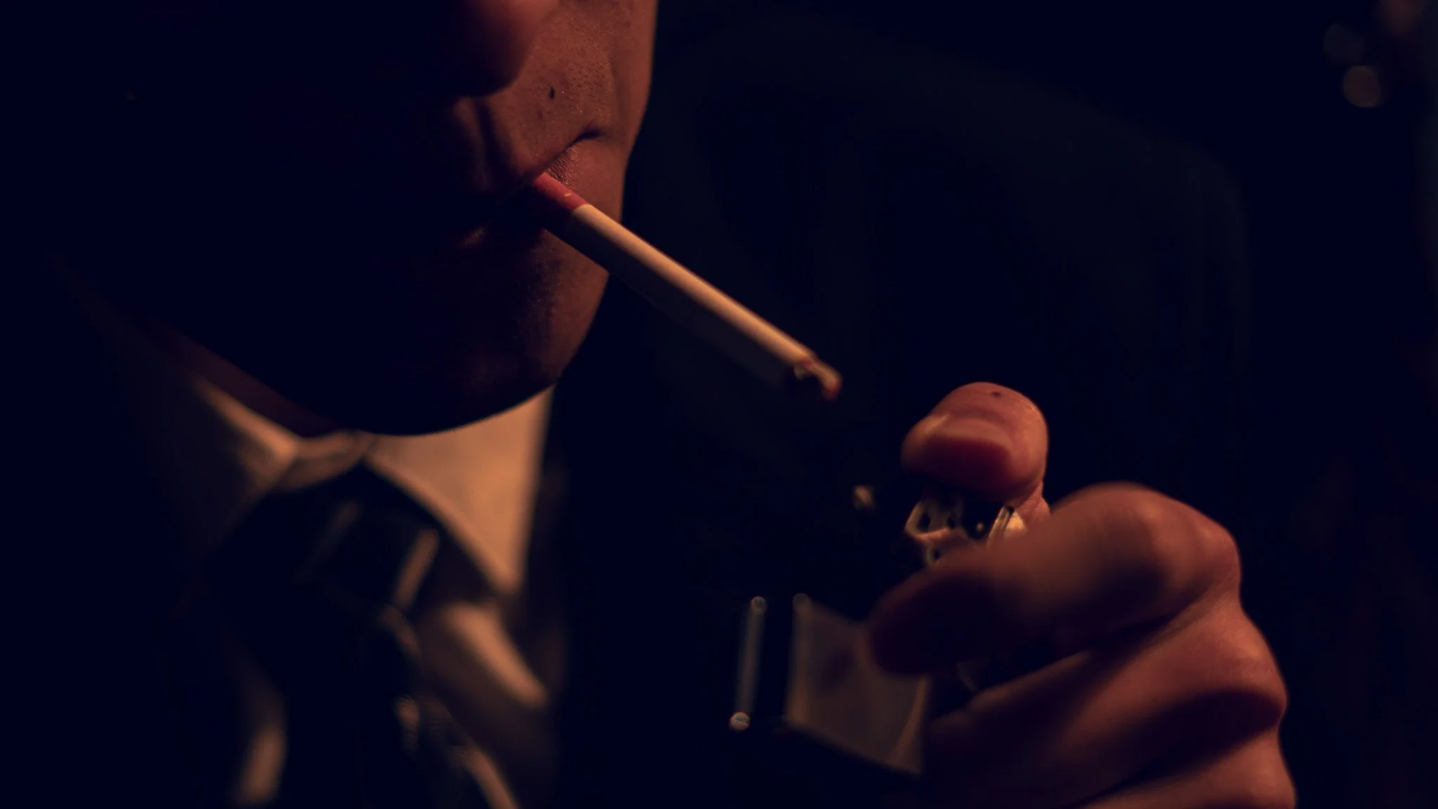 Close-up of a person lighting a cigarette with a lighter in a dark setting.