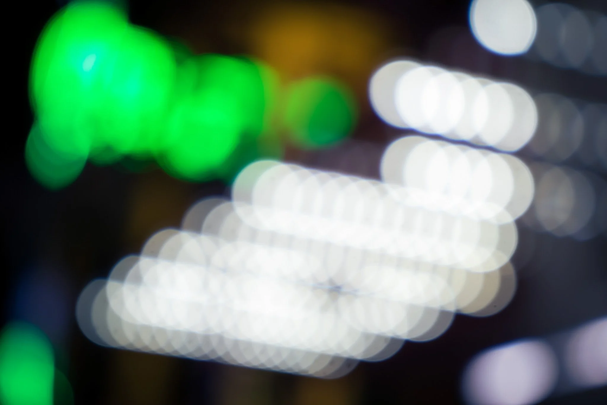 Blurred colorful lights at night, with prominent green and white lights creating a bokeh effect.