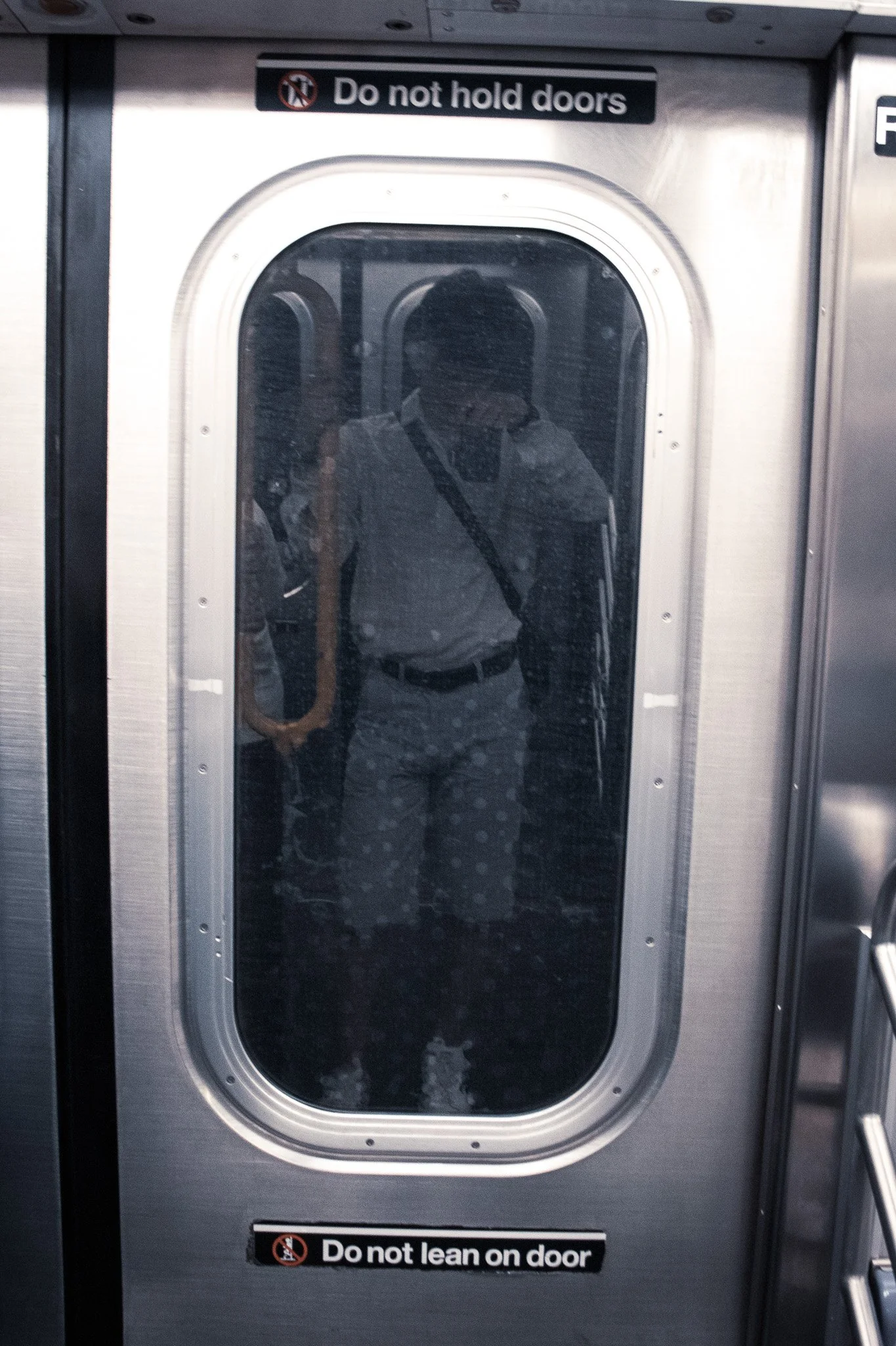 Close-up of a stainless steel door with a window, with a sign that reads, 'Do not hold doors,' and another sign at the bottom that says, 'Do not lean on door'.