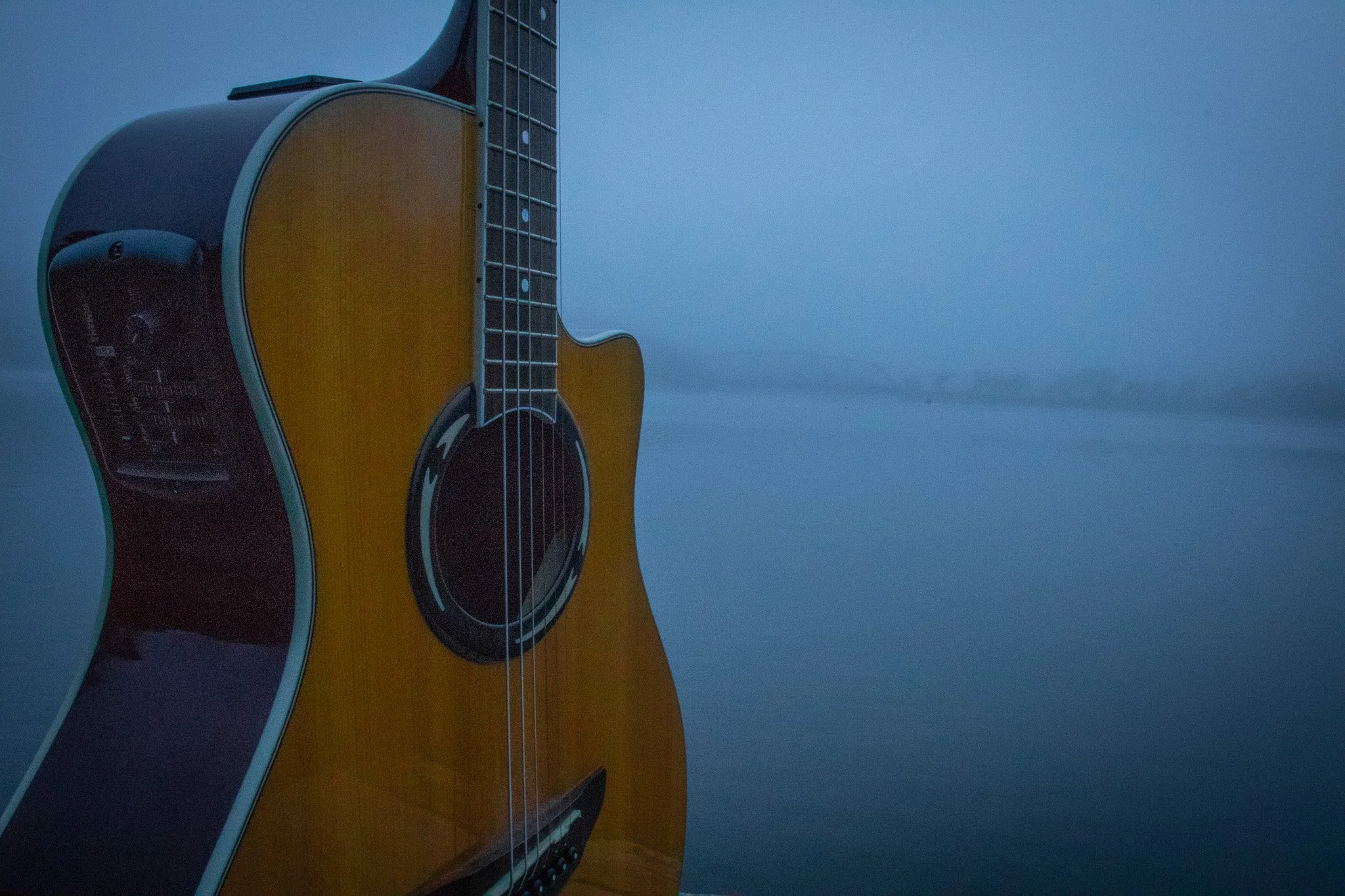 Close-up of an acoustic guitar's body, strings, and fretboard against a light blue background.