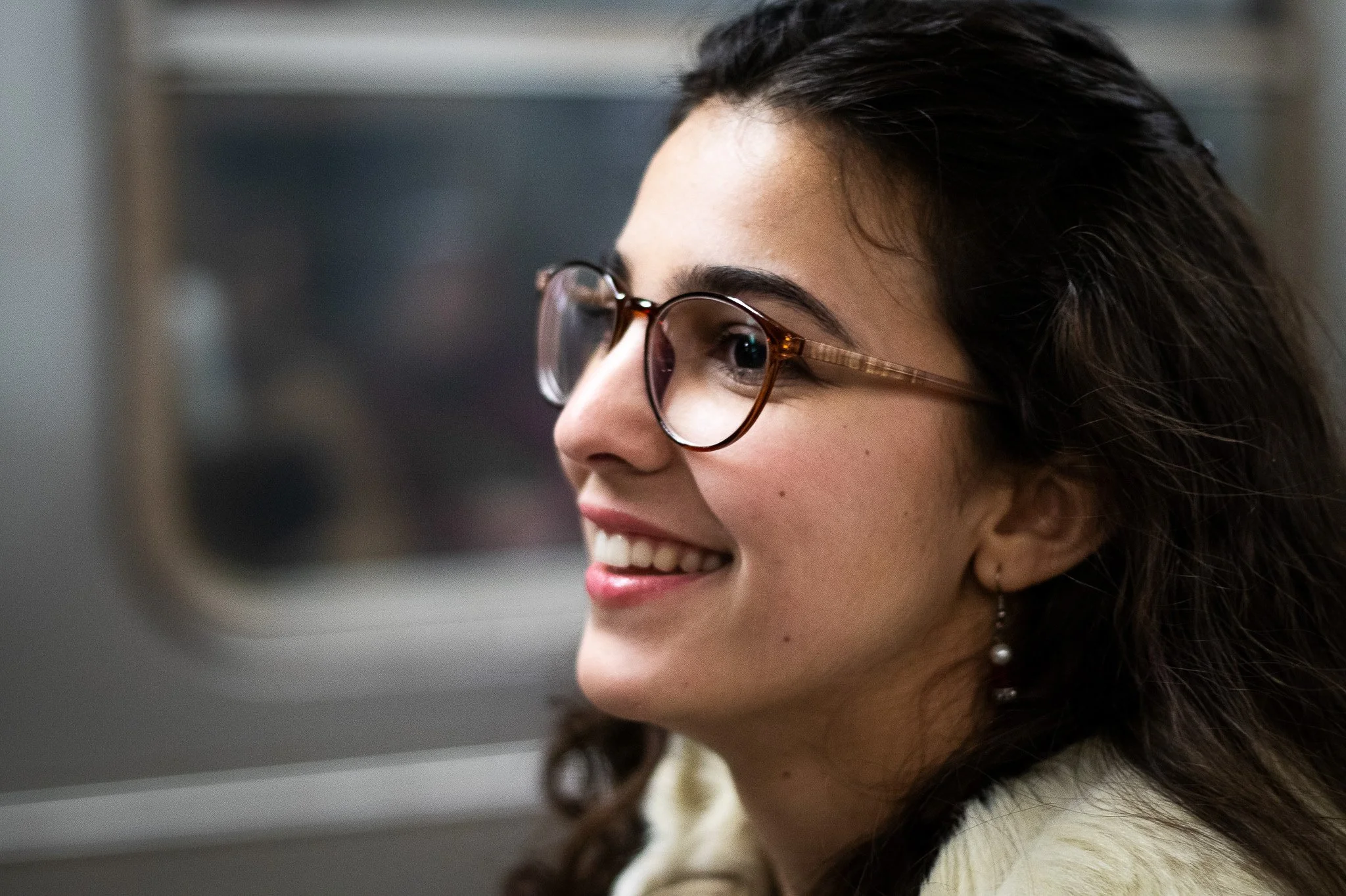 Close-up of a smiling woman with dark curly hair wearing glasses, looking at a computer screen.