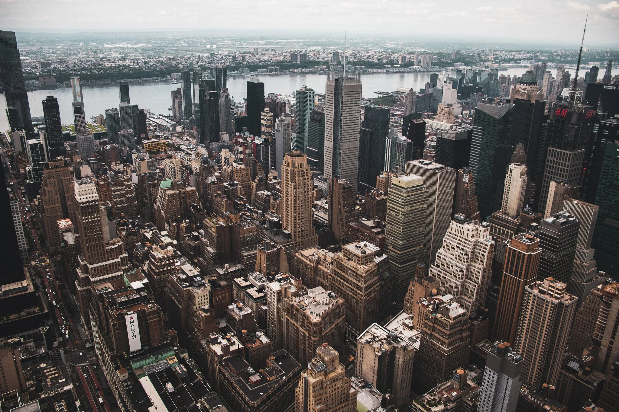 Aerial view of the New York City skyline showing numerous tall buildings and skyscrapers along the river, with some clouds in the sky.