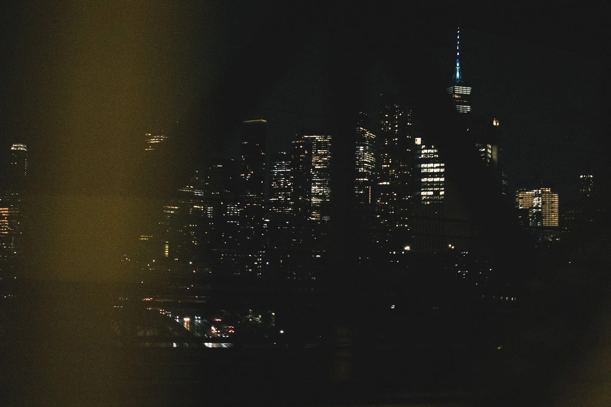 Nighttime city skyline with several illuminated skyscrapers, including a tall tower with a lit spire, against a dark sky.