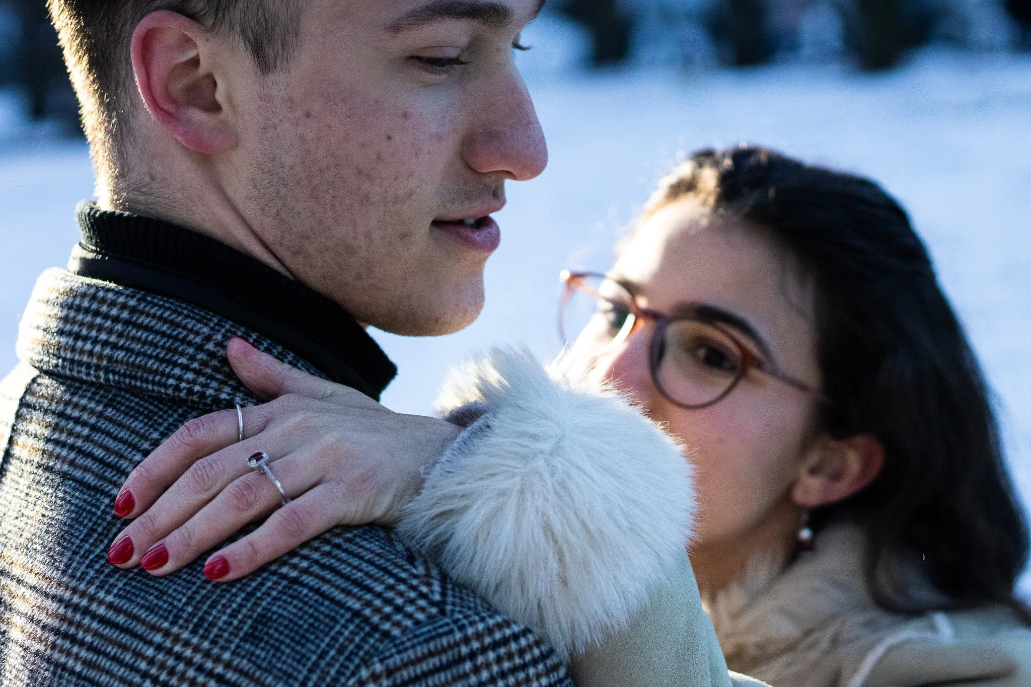A young man and woman hugging outdoors in a snowy landscape.