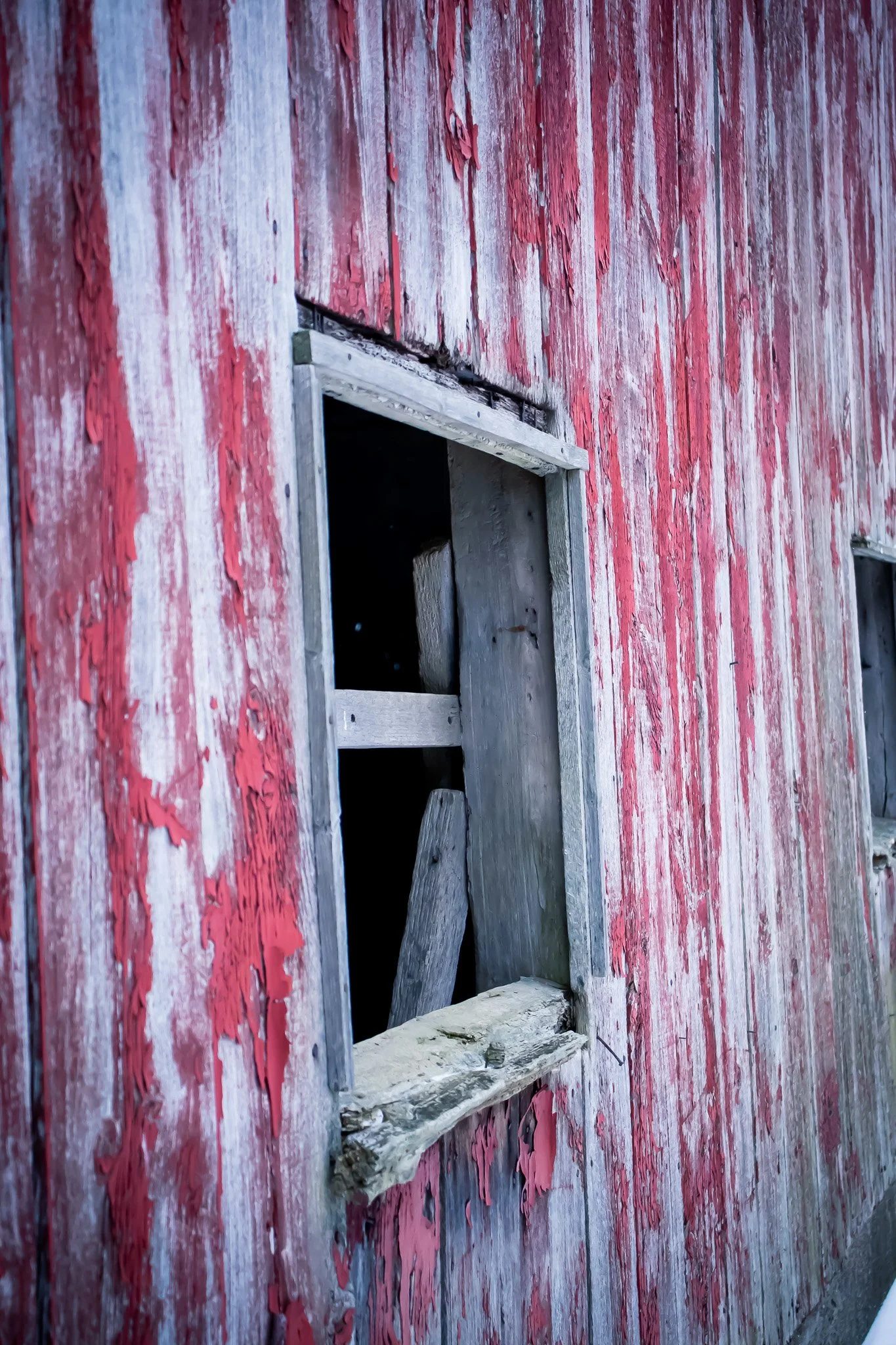 A weathered wooden wall with peeling red paint and a boarded-up window.