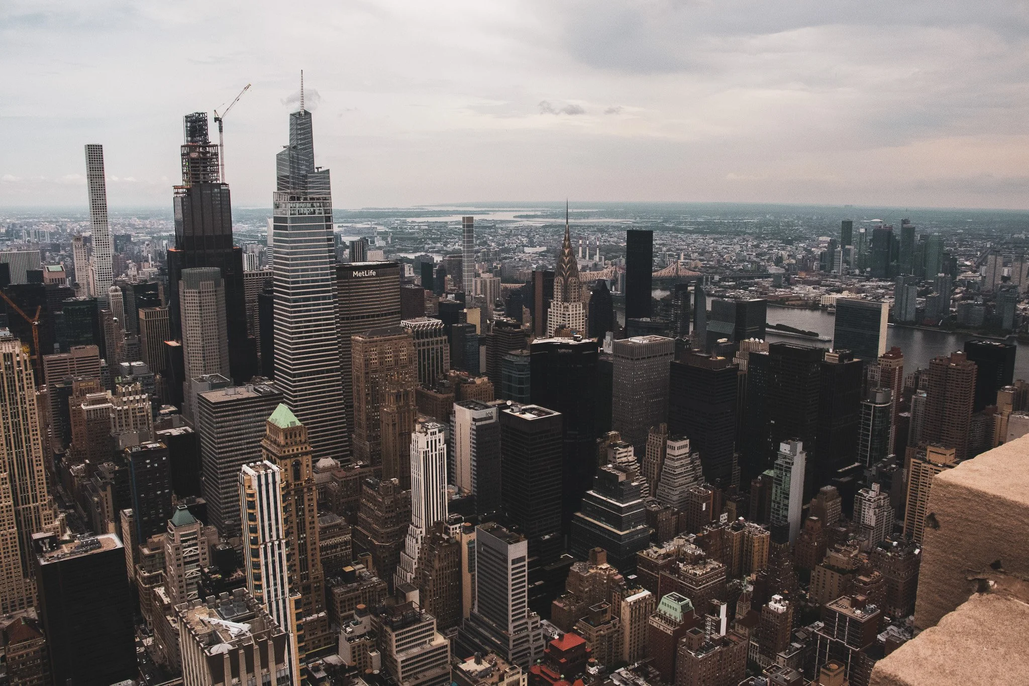 A cityscape view of tall skyscrapers and buildings in a dense urban area, with a river visible in the background and overcast skies above.