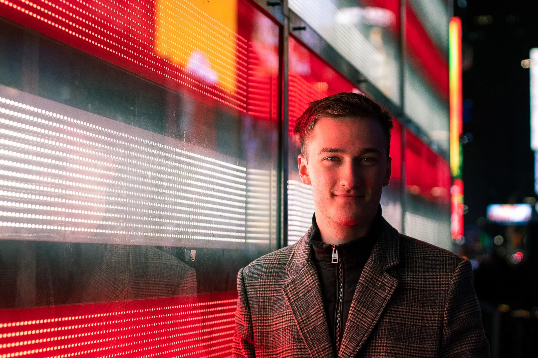 Young man standing next to a brightly lit red and yellow neon sign at night