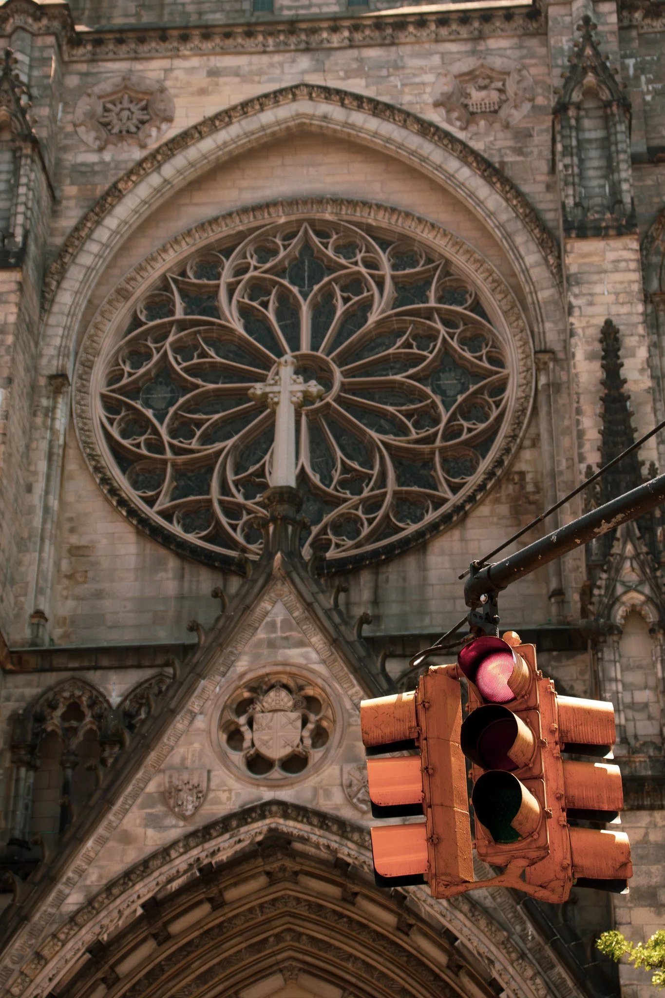 A large stained glass rose window on a gothic cathedral with a traffic light in the foreground.