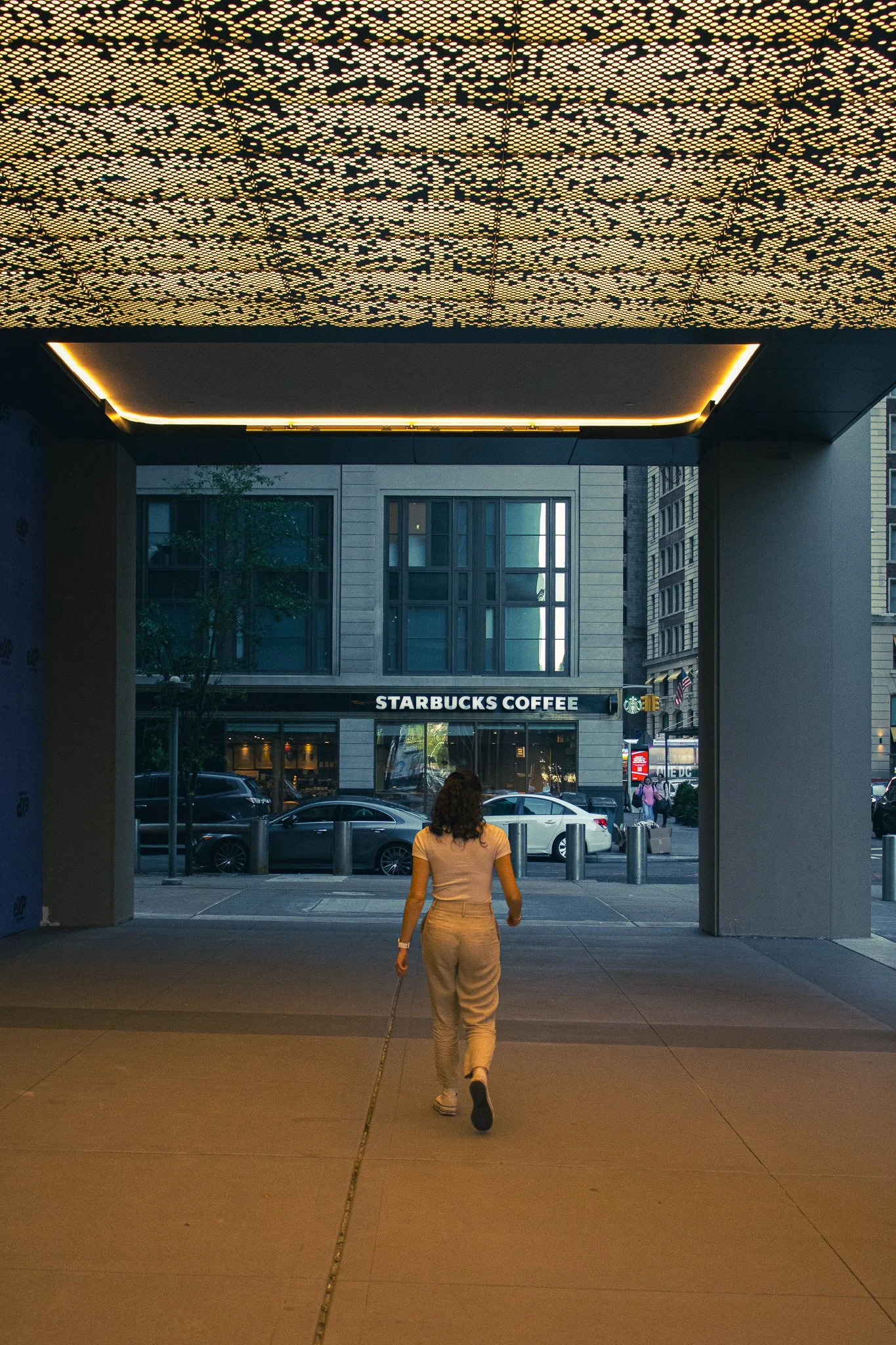 A woman walking out of a building with large glass windows and a Starbucks Coffee sign across the street.