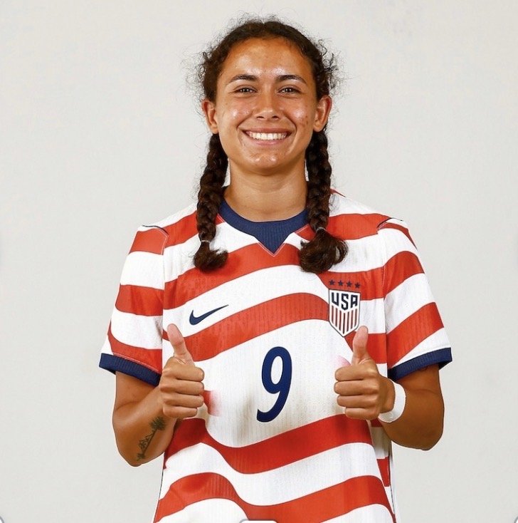 Female soccer player wearing a USA jersey with the number 9, smiling and giving two thumbs up.