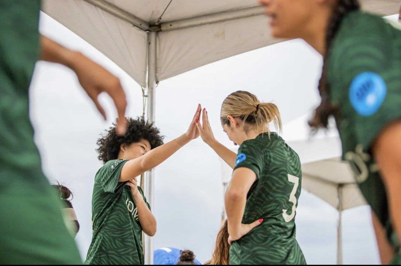 Two female soccer players in green jerseys giving each other a high five during a game or event