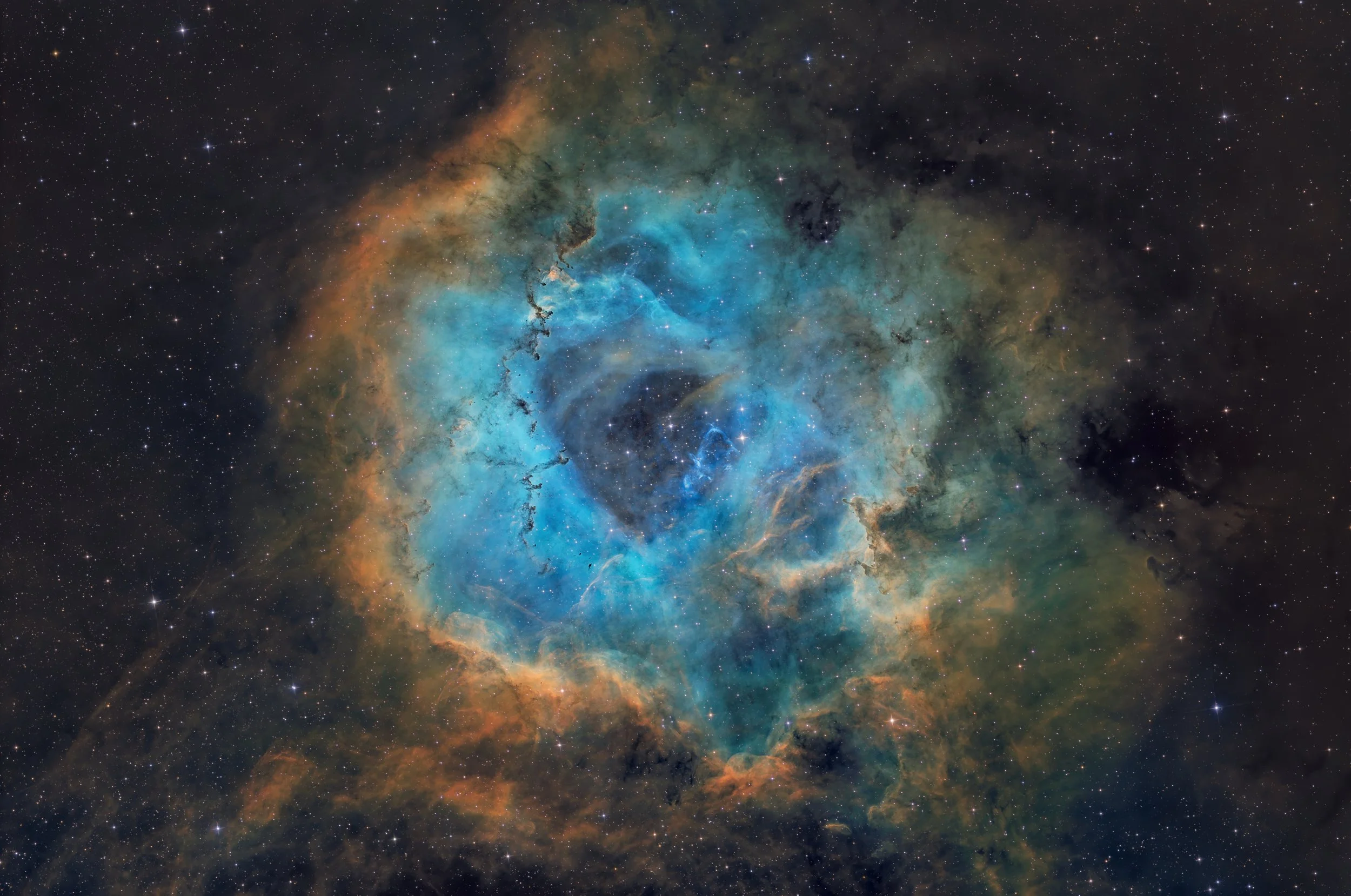 Colorful image of space showing a nebula with bright blues, oranges, and dark regions, surrounded by numerous stars.
