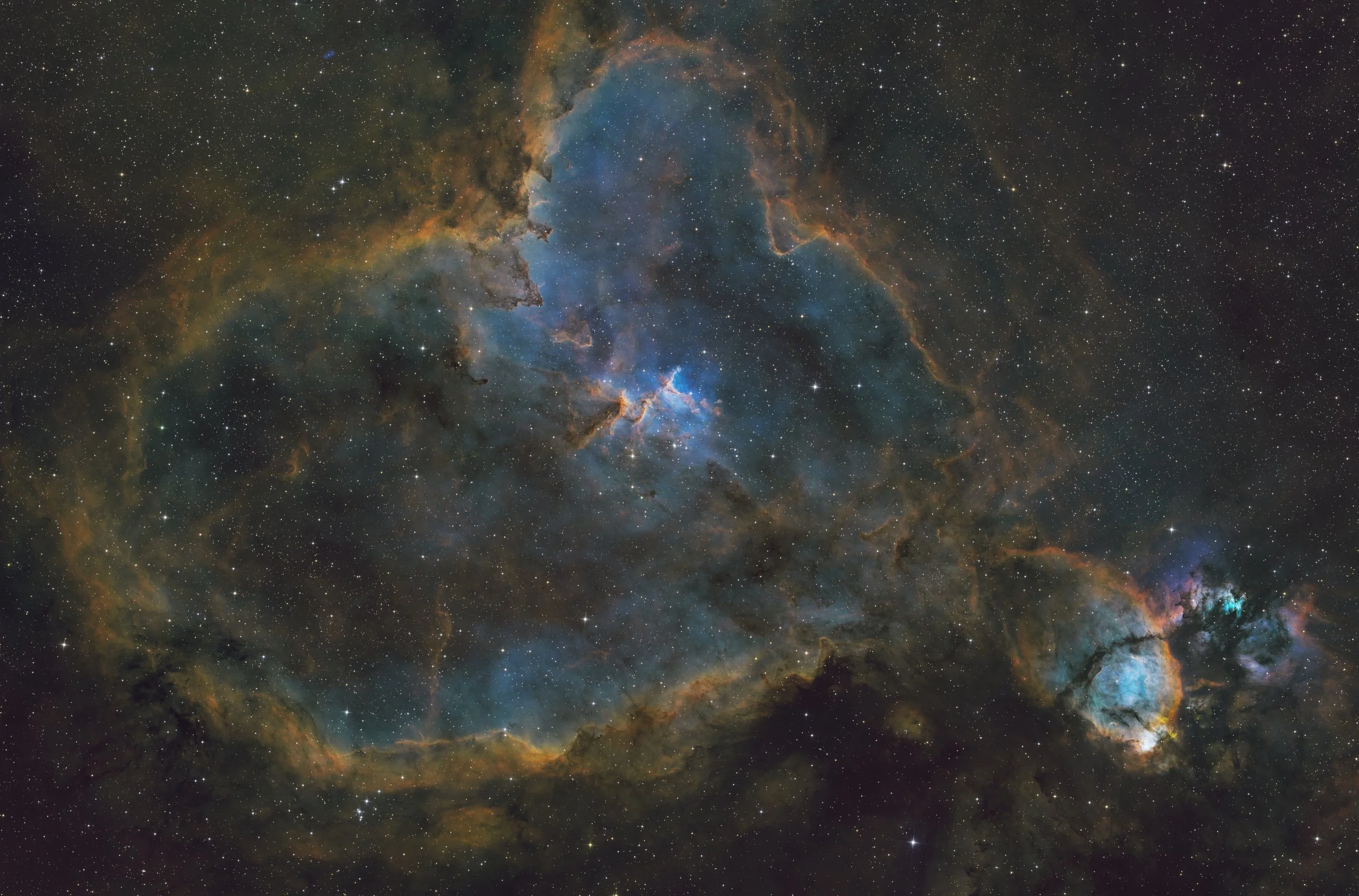 A detailed view of a colorful star-forming nebula with clouds of gas and dust, embedded with numerous stars, against the backdrop of a dark space filled with distant stars.