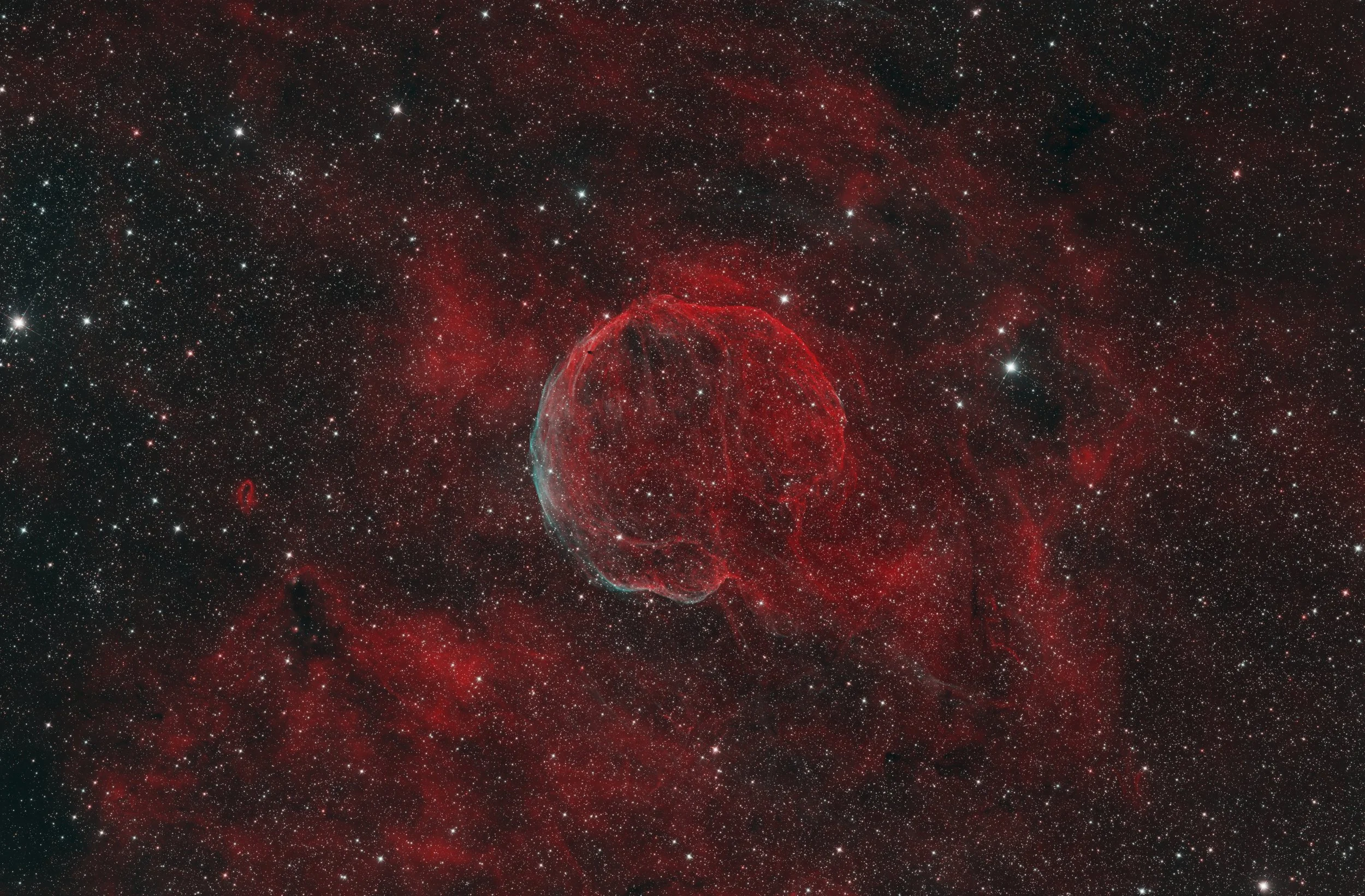 A detailed image of deep space showing numerous stars, red nebulae, and a prominent nebula with bright edges and intricate filaments.