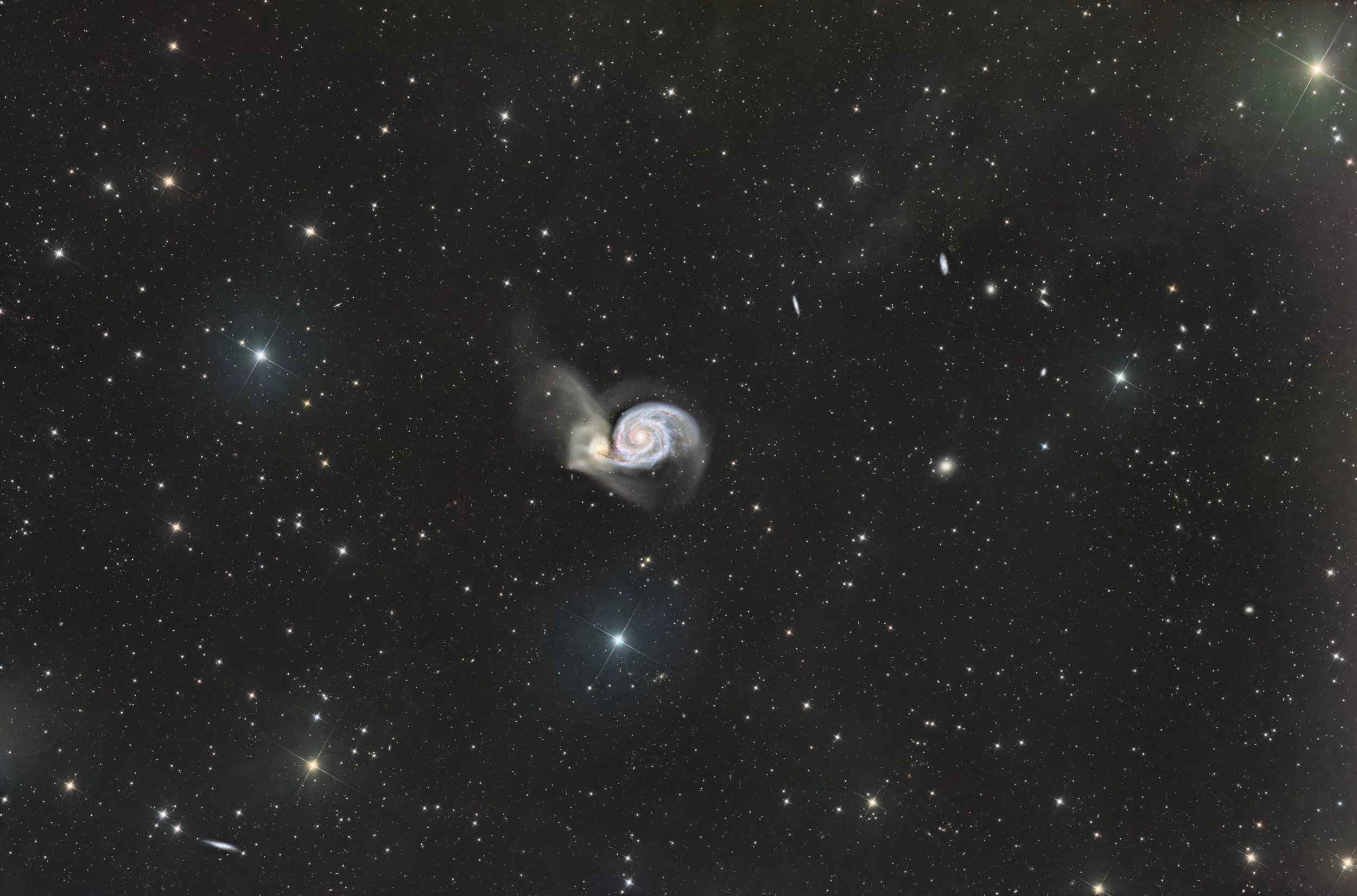 A wide view of outer space with numerous stars, galaxies, and bright celestial objects, featuring a spiral galaxy near the center.