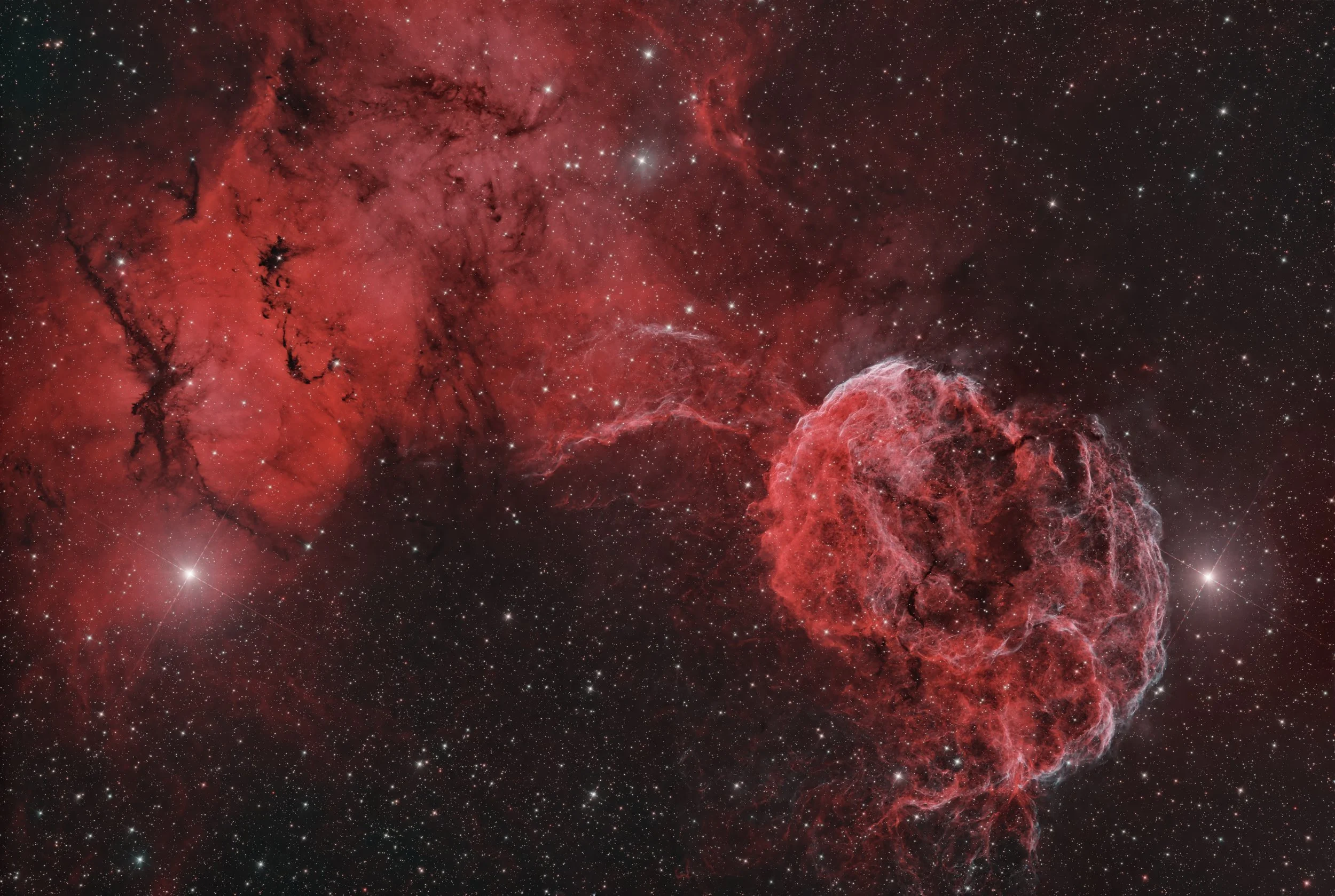 A colorful image of a nebula in space with red and black clouds, numerous stars, and deep space background.