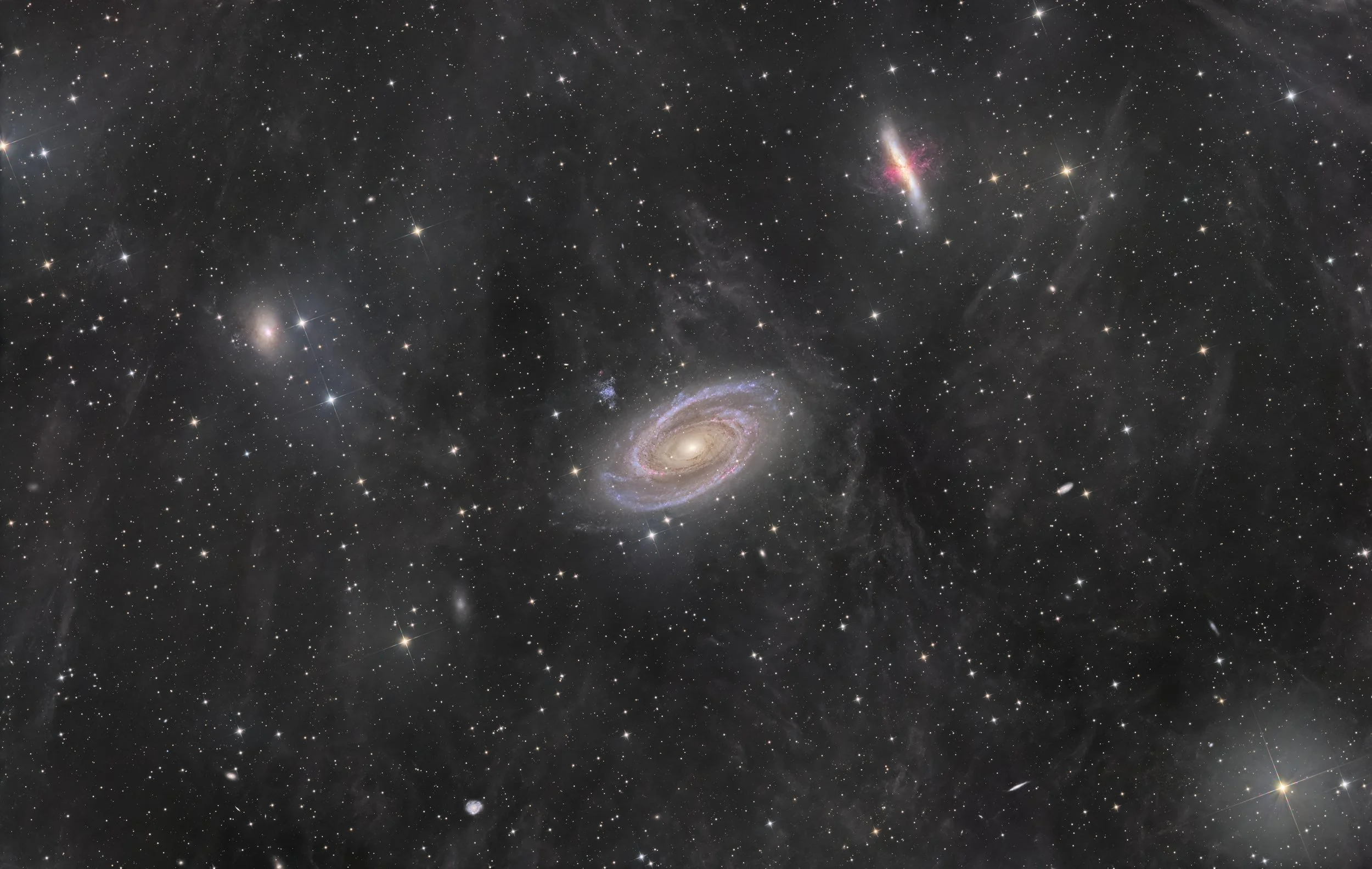 A detailed image of deep space showing numerous stars, galaxies, and cosmic dust, including a spiral galaxy with bright core and pinkish arms.
