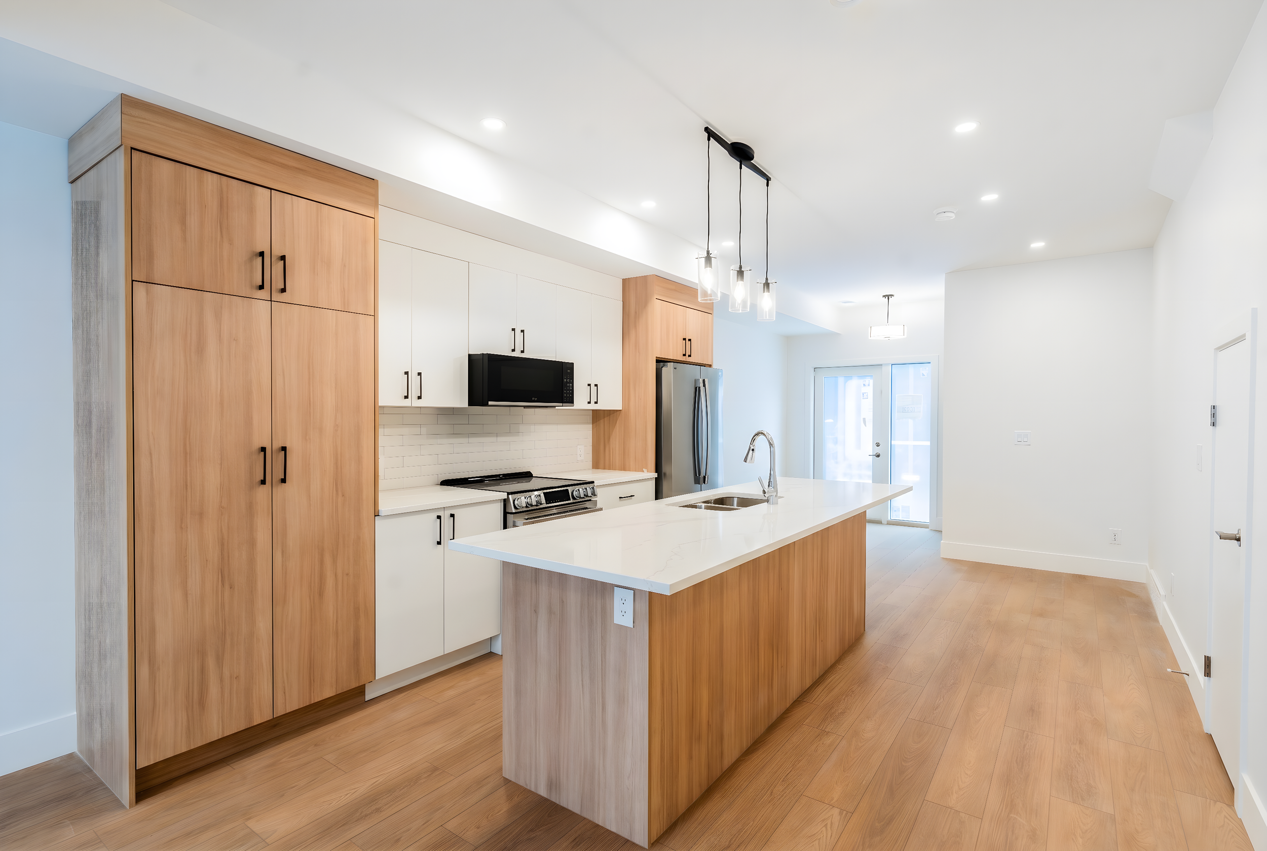 Unit 101 Uptown 17th Calgary 3-bed townhouse kitchen with two-tone wood cabinetry, stainless steel appliances, white quartz island and pendant lighting - available at Suite Getaways
