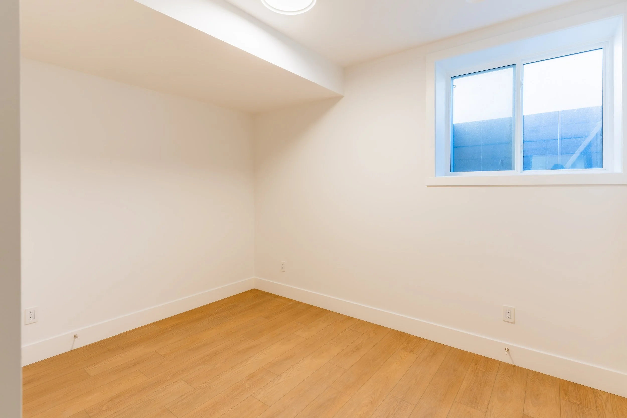 Empty lower suite bedroom with hardwood floors and window in Unit 204R Uptown 17th Calgary 1-bedroom lower suite rental near 17th Ave SW by Suite Getaways