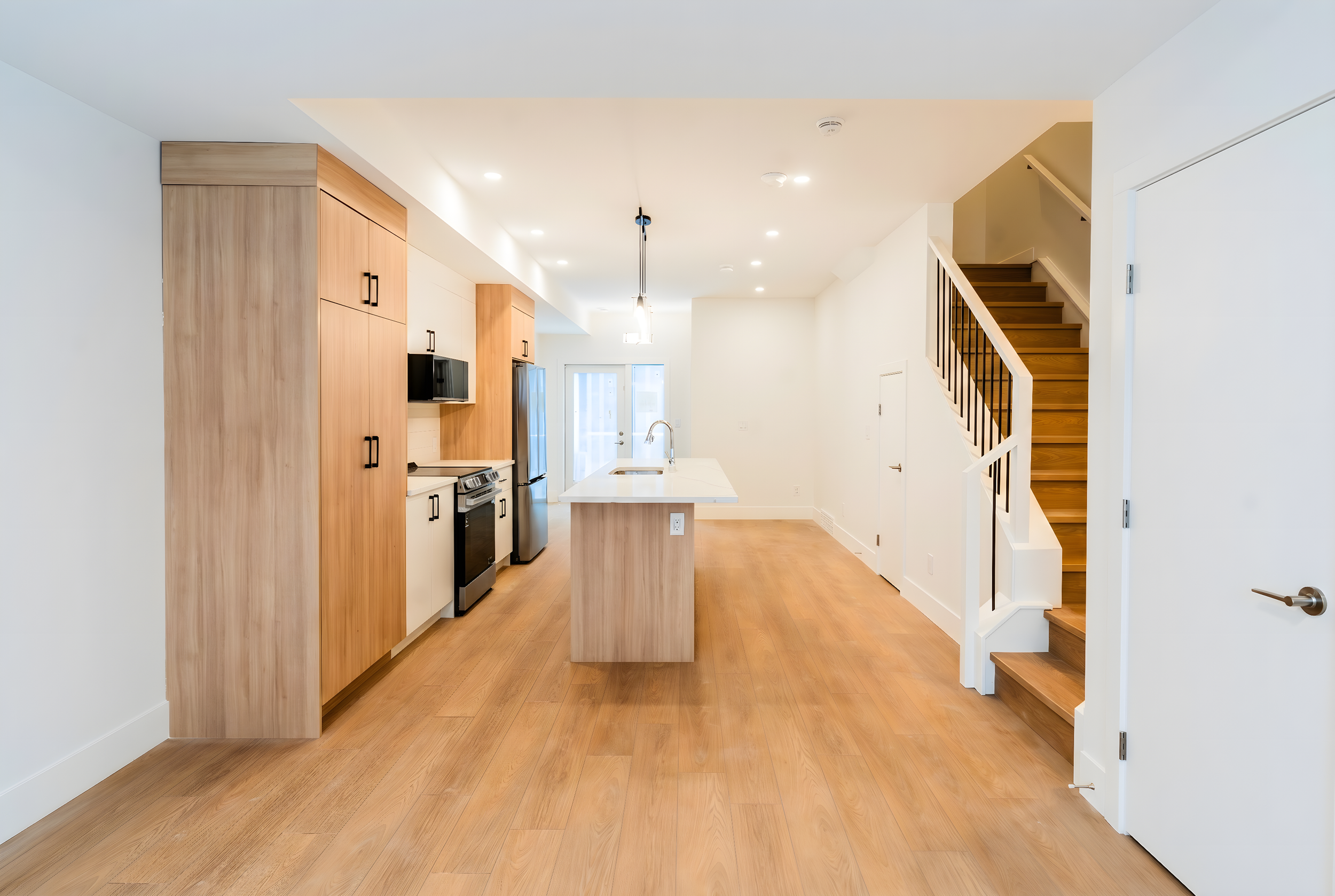 Open-concept kitchen and living area with wood cabinetry, LG appliances and staircase at Uptown 17th Calgary rental suites near 17th Ave SW by Suite Getaways