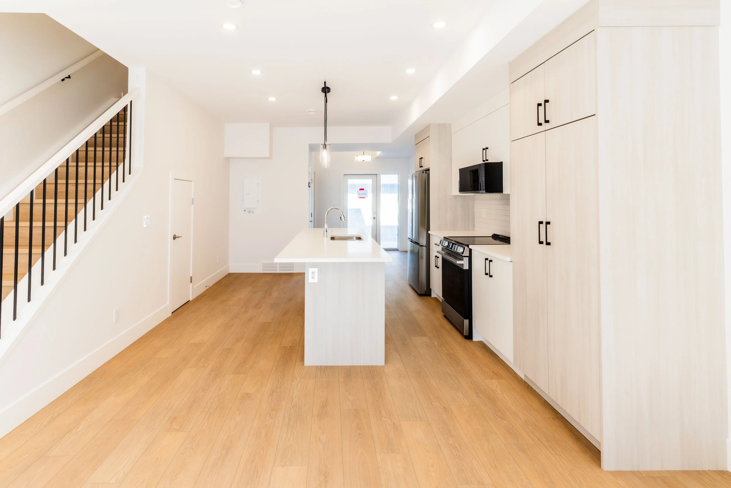 Unit 203 Uptown 17th Calgary 3-bed townhouse open-concept kitchen with white island, pendant lighting and staircase - available at Suite Getaways