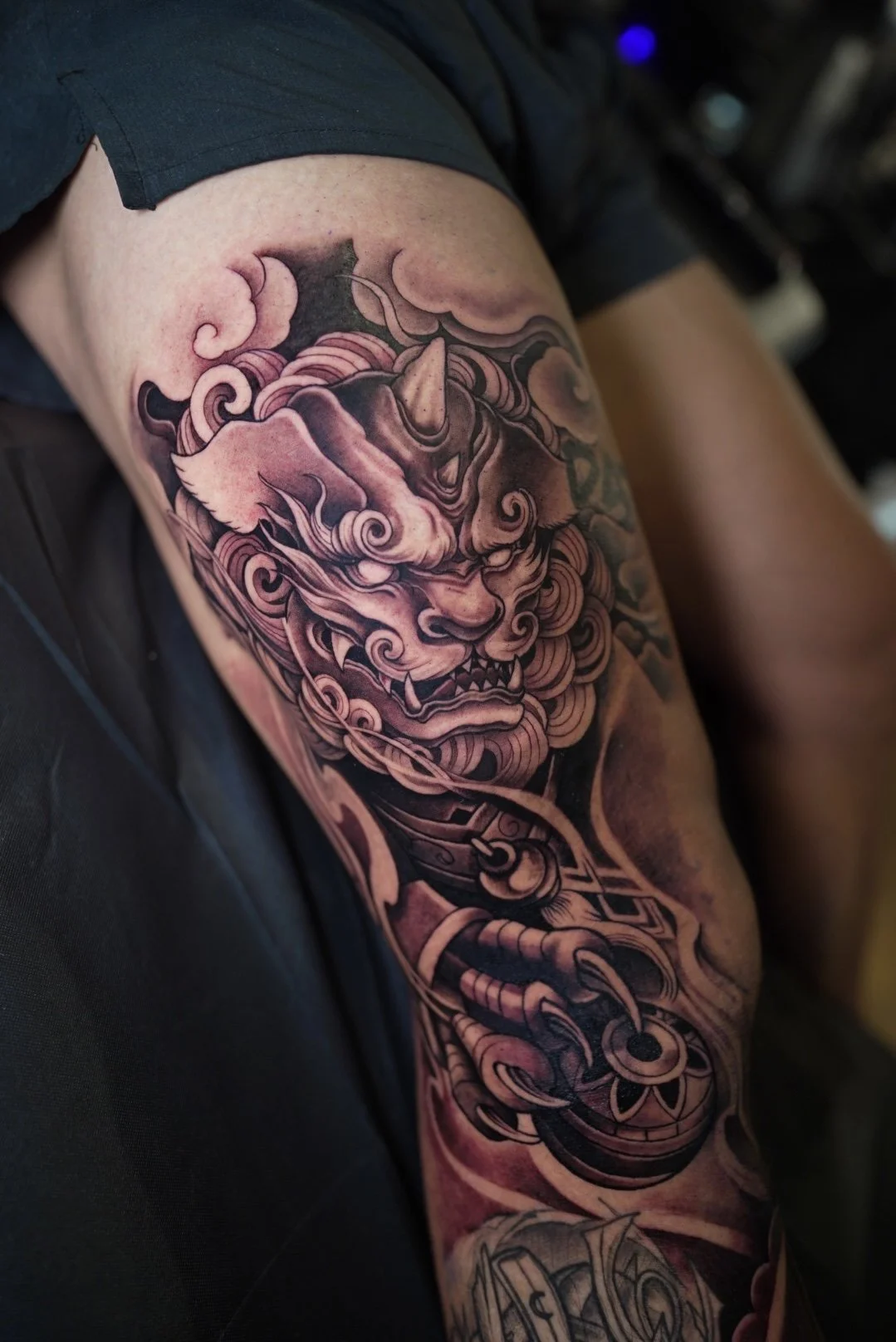 Tattoo of a fierce, traditional Asian lion with flowing mane on a person's upper arm.