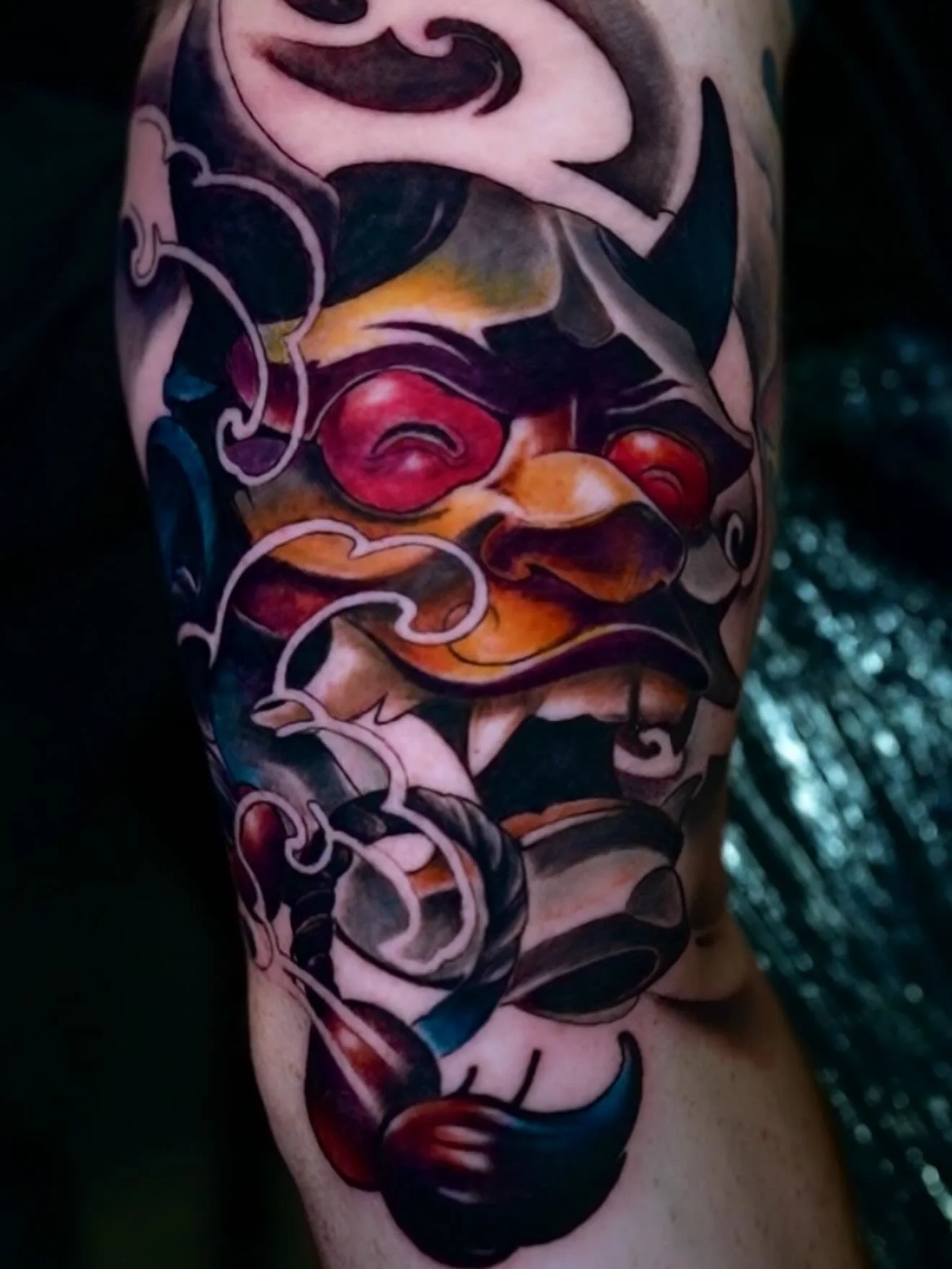 Colorful tattoo of a traditional Japanese-style demonic face on a person's arm with bold lines and vivid colors.