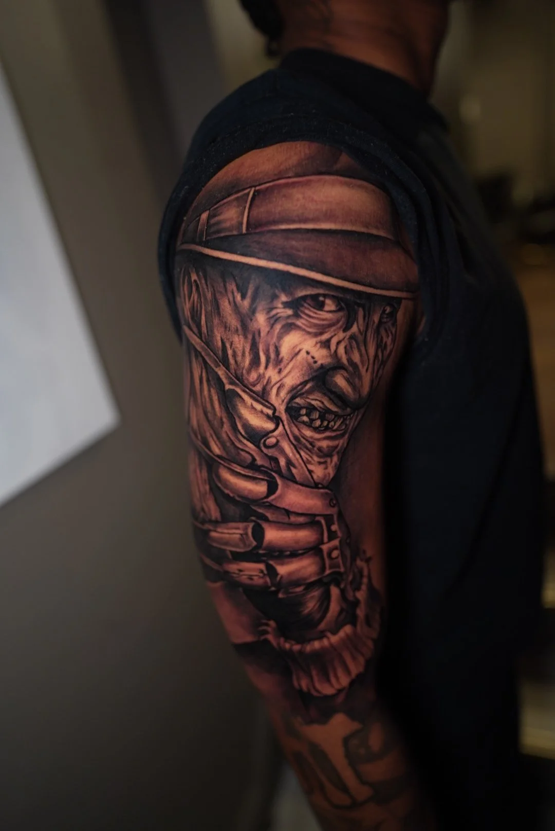 Black and gray tattoo of a snarling dog wearing a hat, holding a pistol, on a person's upper arm.