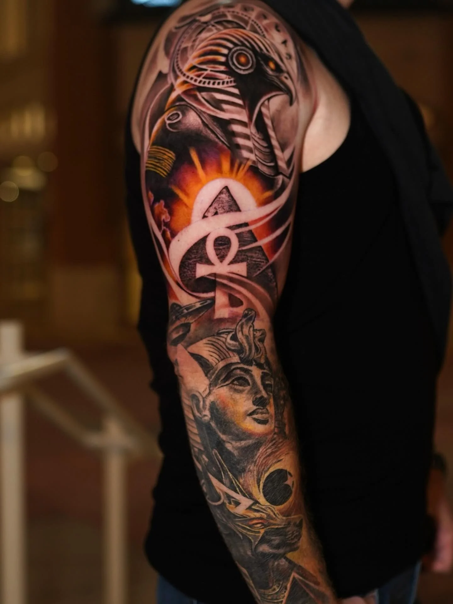 Close-up of a person's upper arm tattoo, featuring an eagle, sunrise, and portrait of a woman with long hair.