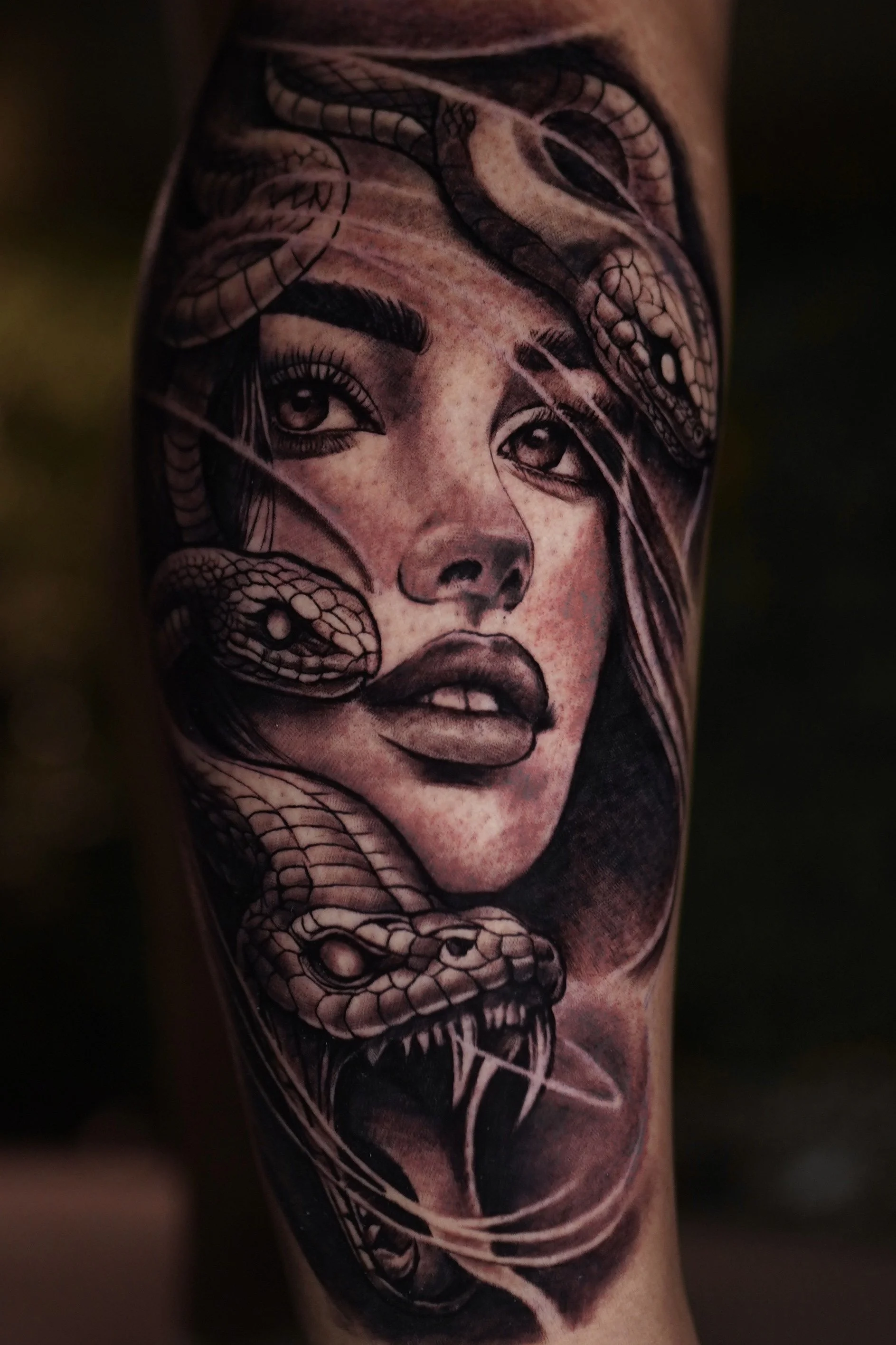 Black and gray tattoo of a woman's face with snakes intertwined around her head and neck.