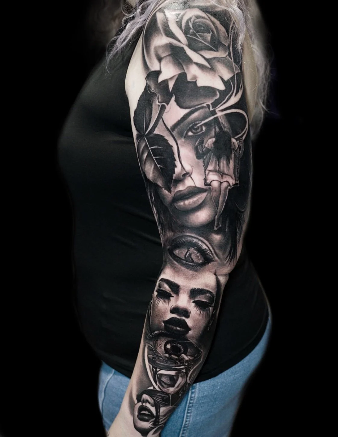 Black and gray tattoo sleeve featuring various emotionally expressive female faces, a rose at the top, and other detailed elements.