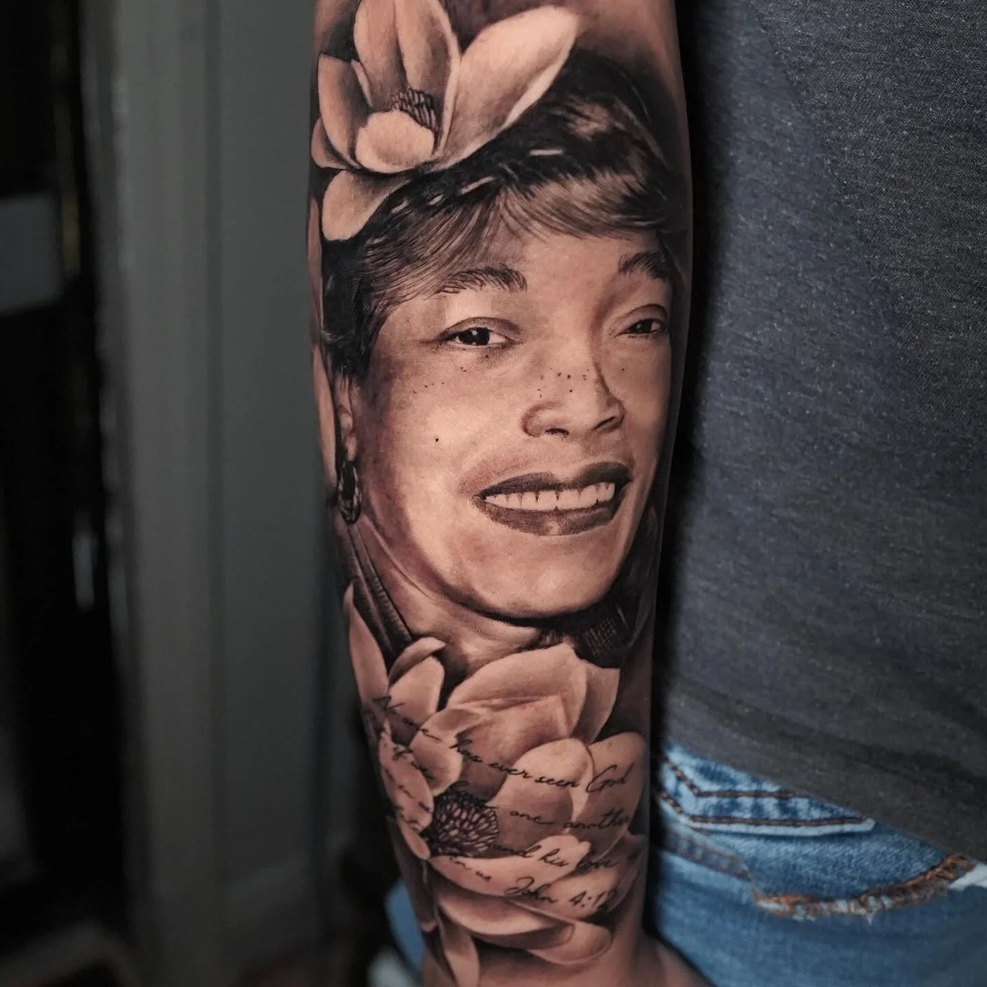 Tattoo of a smiling woman's face with short hair and a floral headband on an arm, with cursive text below.
