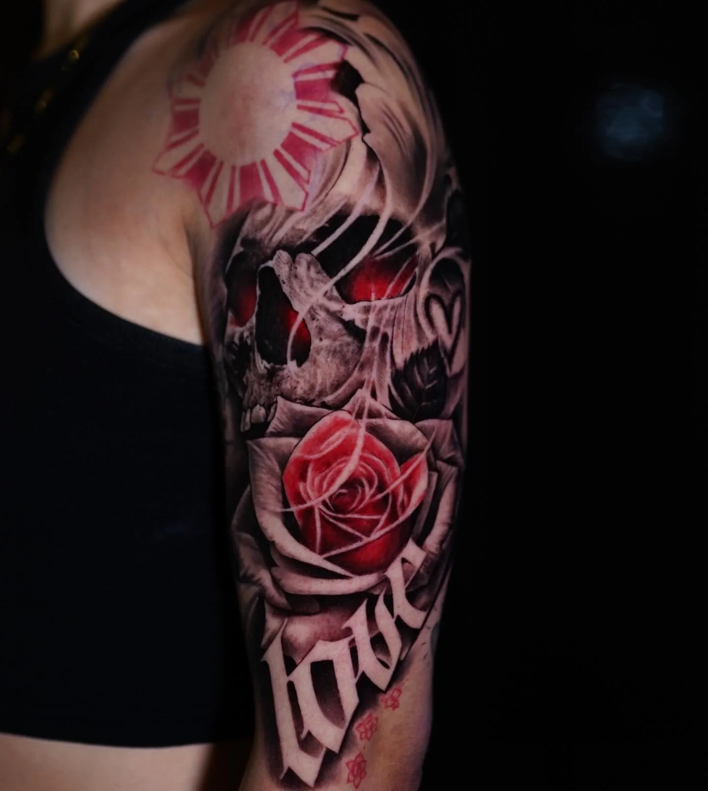 Tattoo of a human heart, skull, and rose on a person's arm with red accents and black background.