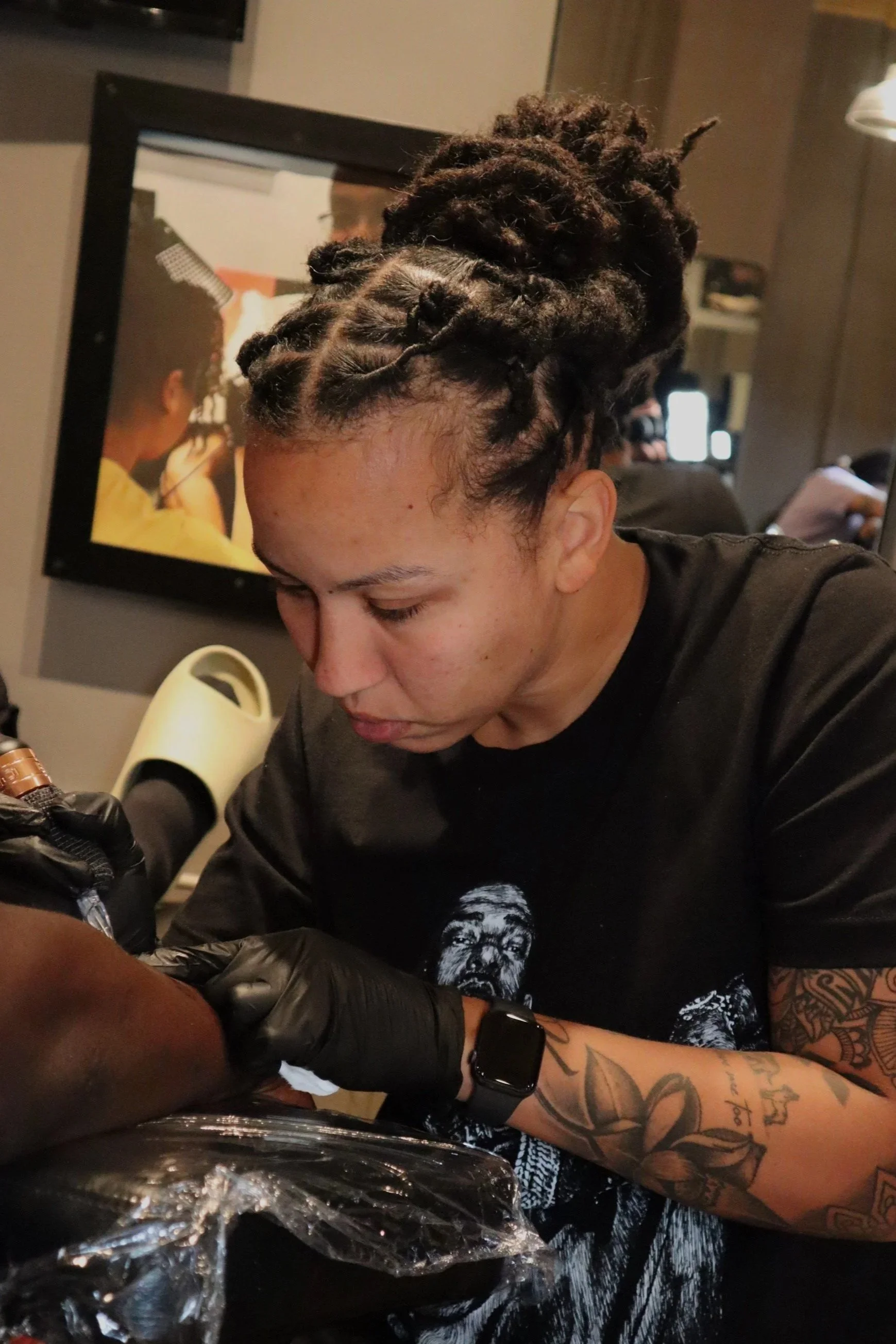 Woman with styled dreadlocks getting a tattoo while wearing black gloves.