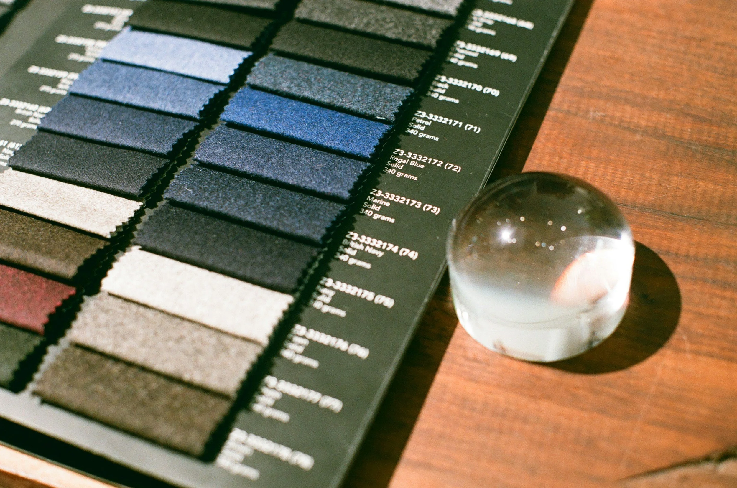 A color palette swatch book with various shades of blue, gray, and black, laid out on a dark surface, with a clear glass sphere nearby.