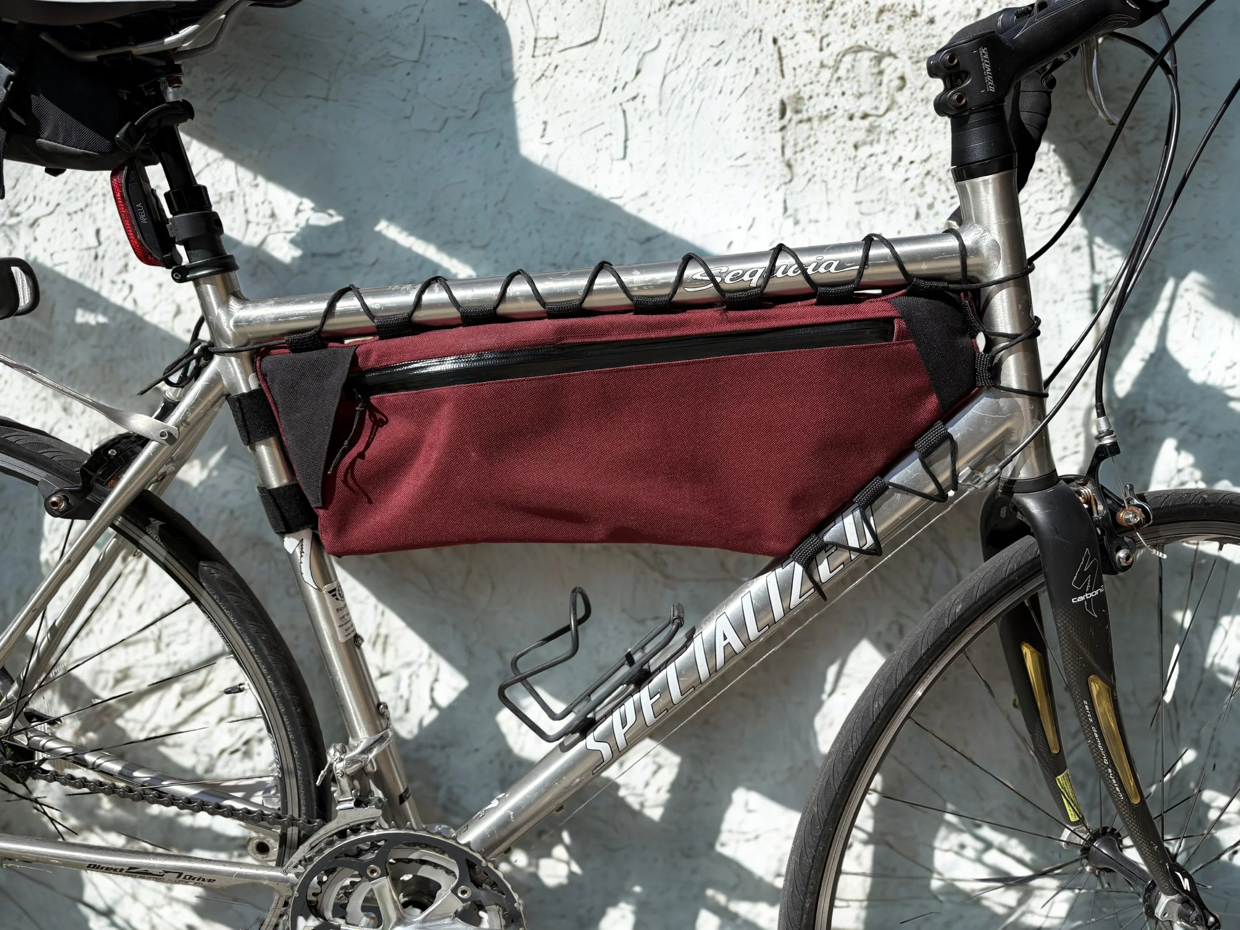 A silver mountain bike with a red bag attached to the top tube, black handlebars, and a black saddle, parked on a white textured surface.