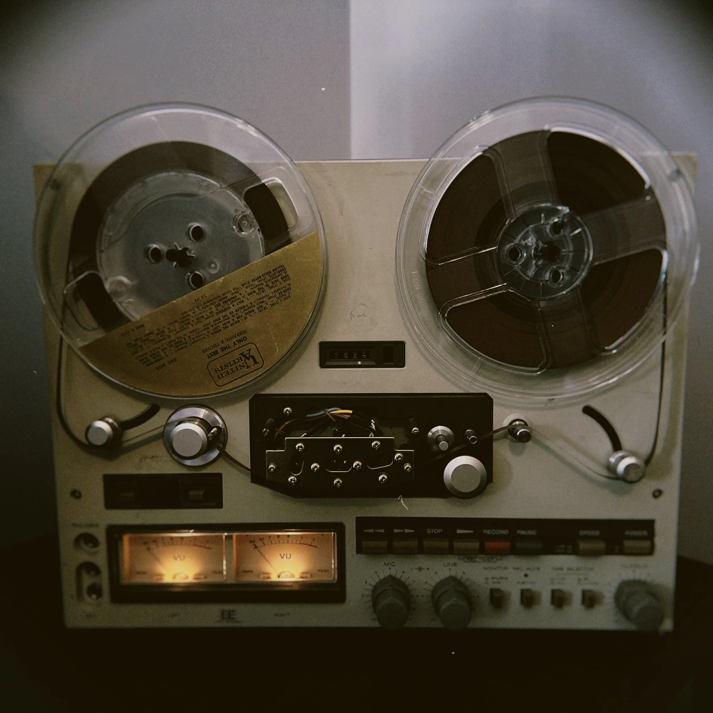 Close-up of a vintage audio reel-to-reel tape recorder, showing two reels of magnetic tape on a metallic device with controls and meters.