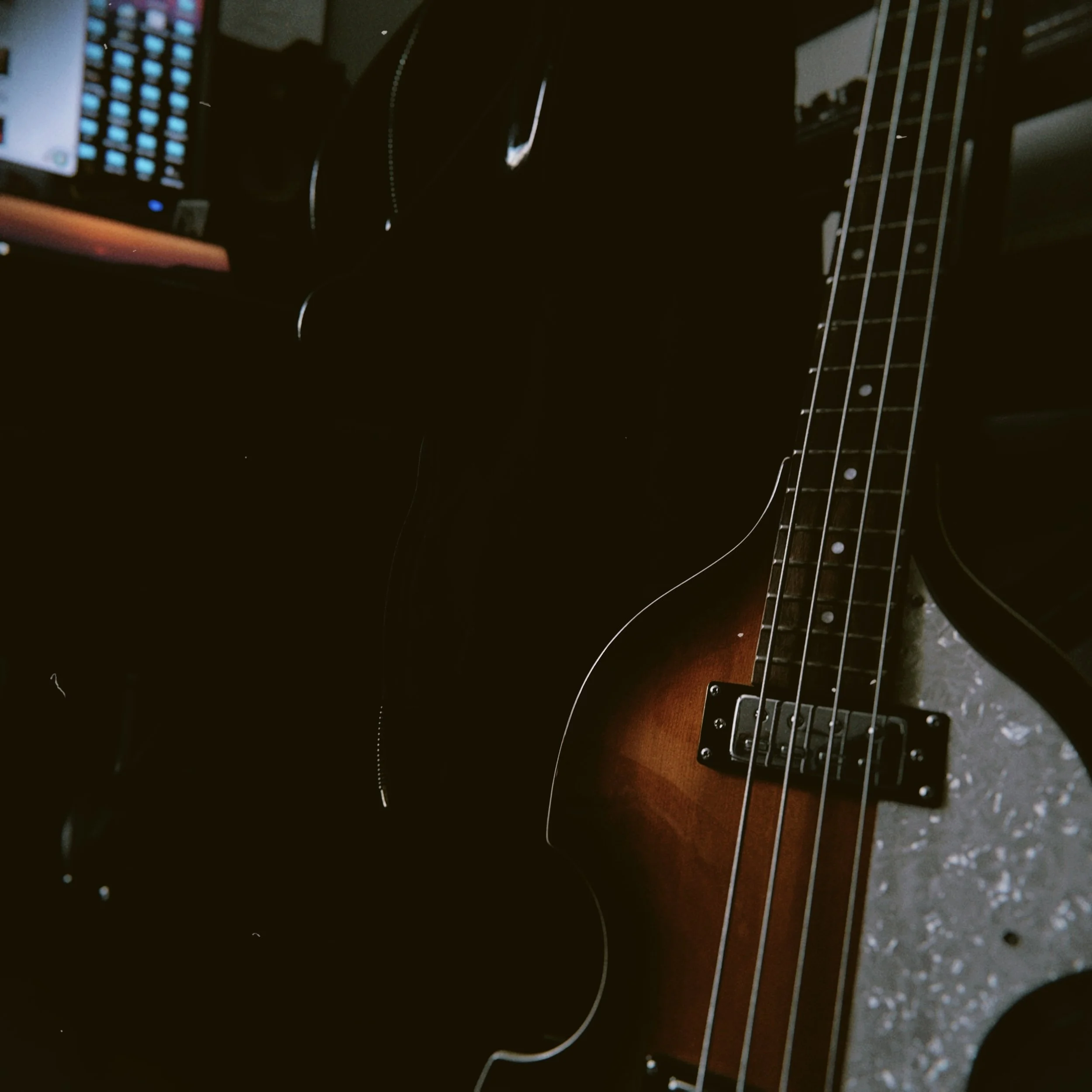 Close-up of an electric guitar with a sunburst finish, strings, and fretboard. Part of a keyboard and a computer screen with blue icons are visible in the background.
